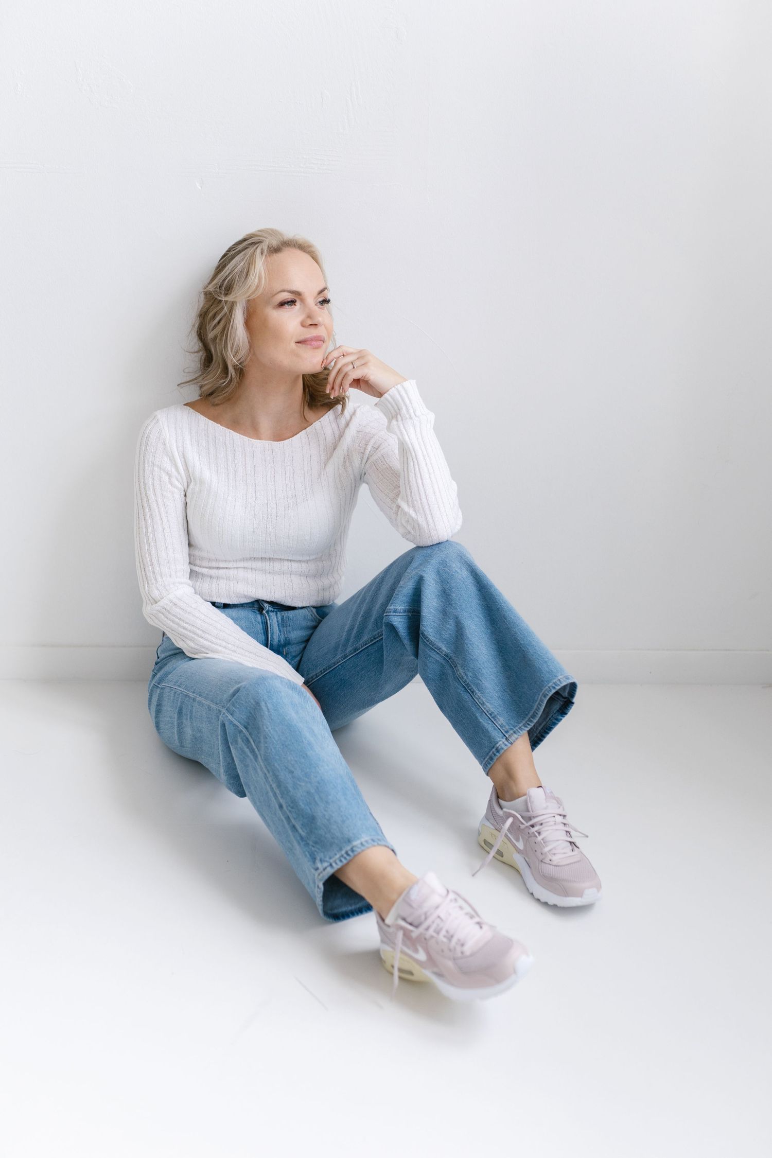 Casual lifestyle photos of someone relaxing on floor wearing white sweater, jeans and pink sneakers.