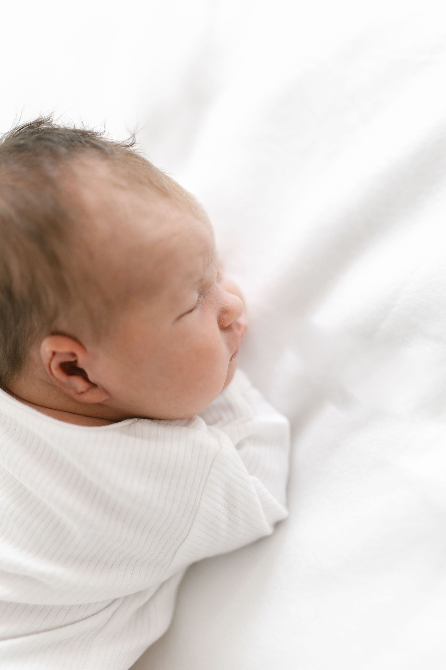 Sleeping newborn in white clothing against light background.