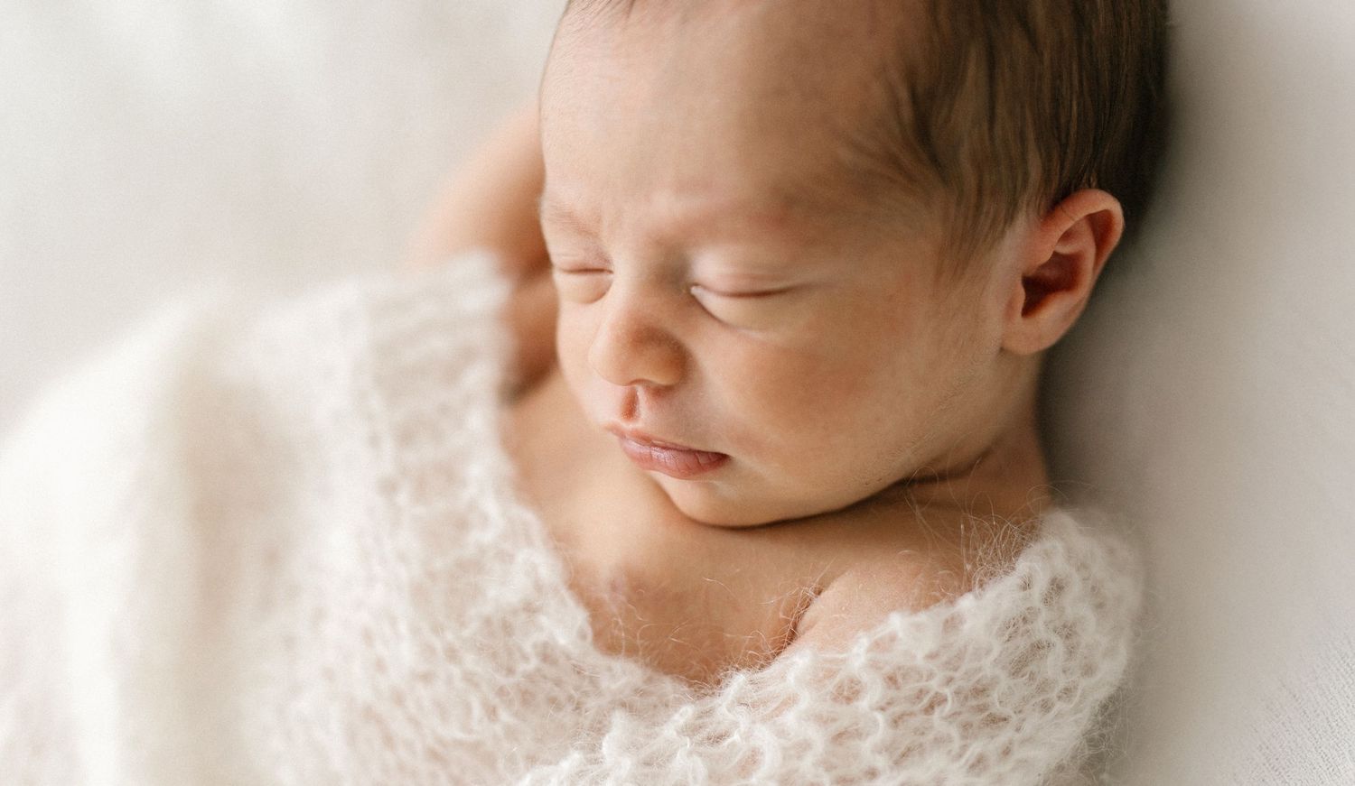 A peaceful newborn baby sleeping wrapped in a soft white knit blanket, captured in a serene studio portrait.