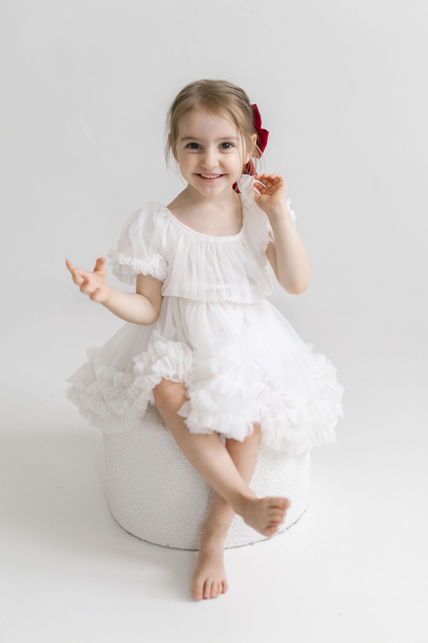 A dancer in a flowing white dress poses playfully on a light background.
