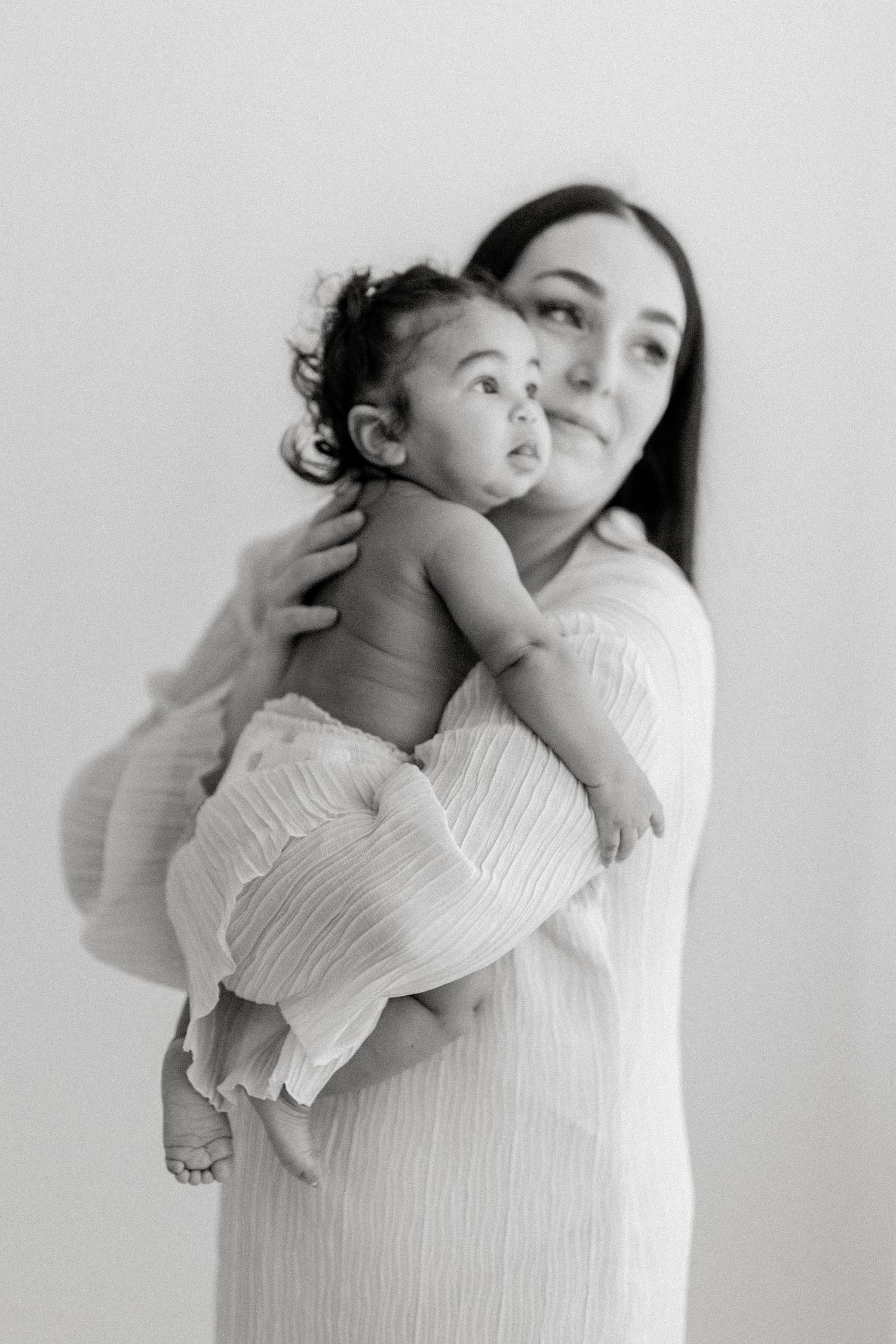 Black and white portrait of a mother in a white dress tenderly holding her newborn baby.