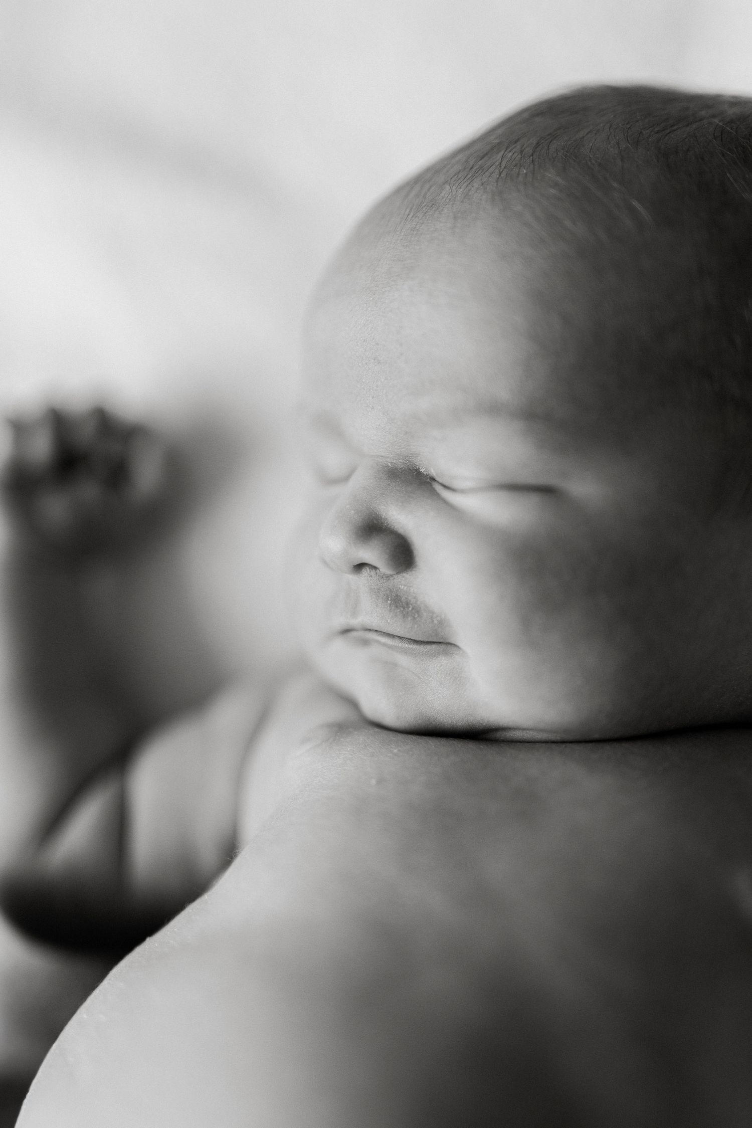 Black and white photo of a peaceful sleeping newborn baby resting their head on an adult's shoulder.