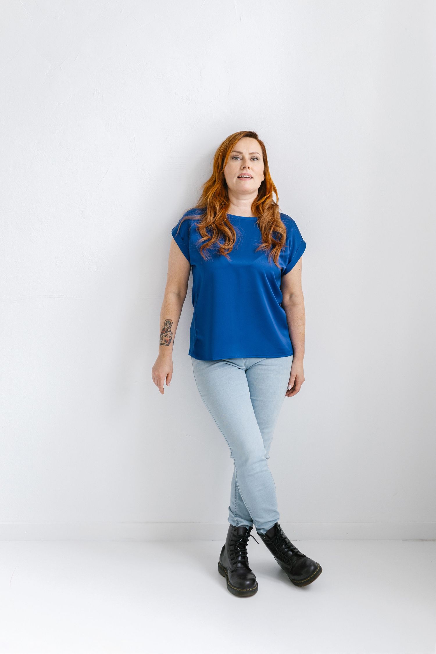 A person in a bright blue top and light jeans poses in different positions against a white studio backdrop.