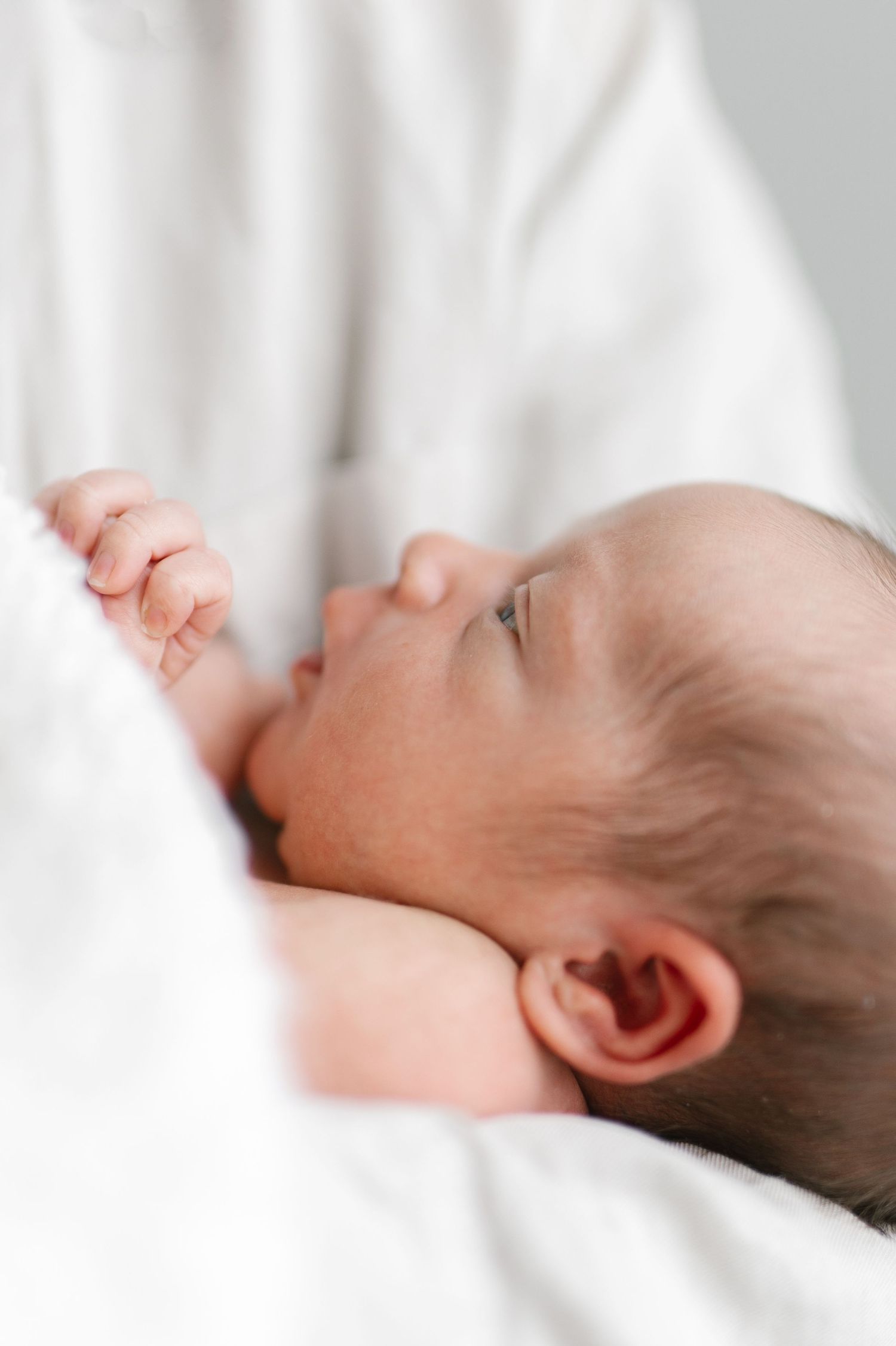 Close-up profile view of a sleeping newborn baby on white bedding.