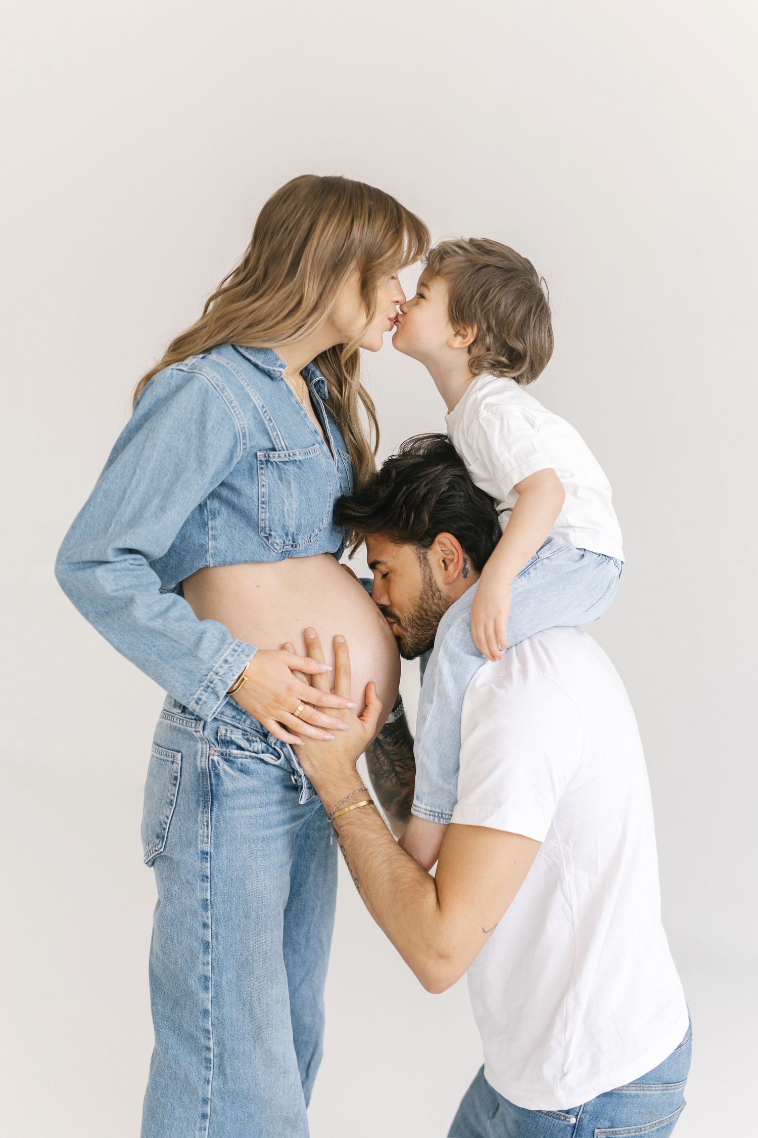 Family maternity photo showing tender moment with pregnant mother in denim and toddler.
