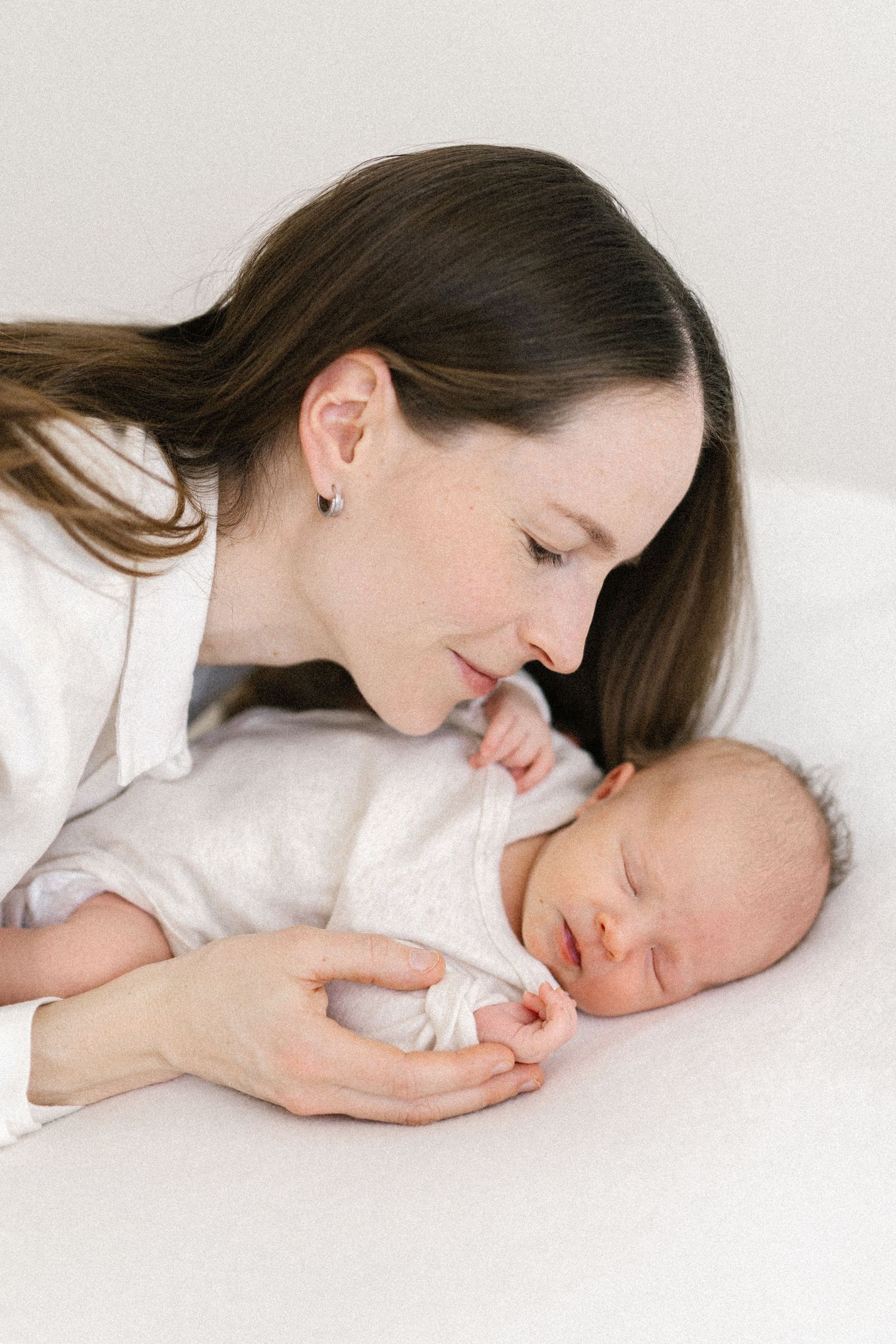 Side view portrait of parent and sleeping newborn in soft white setting.