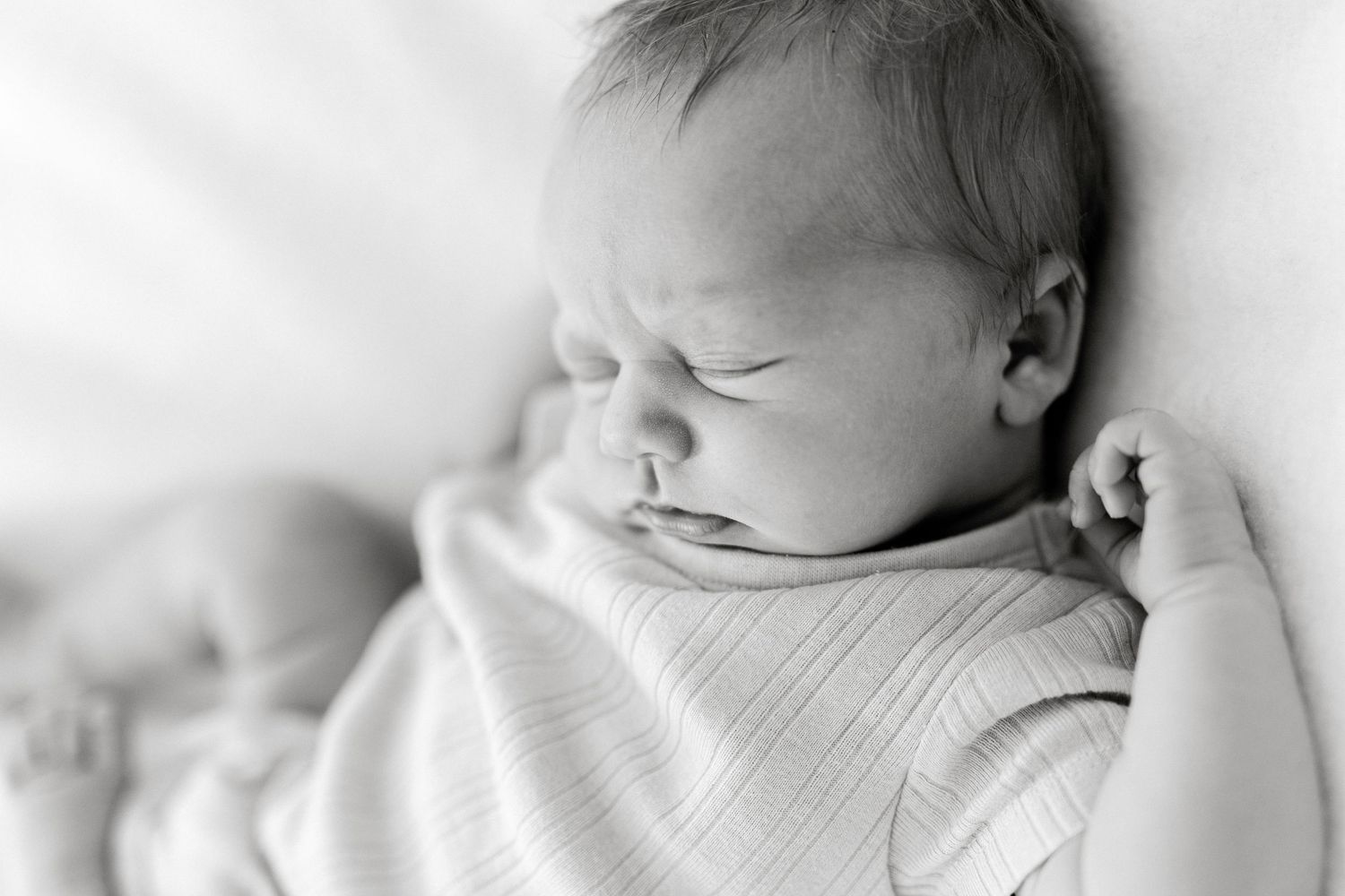 Black and white newborn baby sleeping peacefully, wrapped in soft blanket, close-up portrait photography.