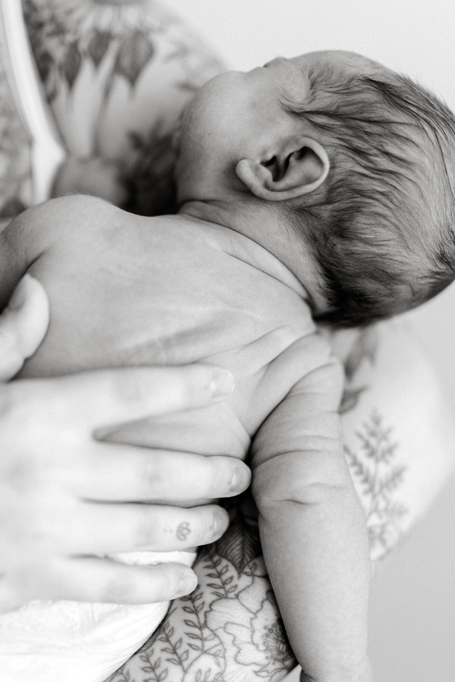 Black and white photo of a newborn baby being cradled in the arms of a tattooed parent.