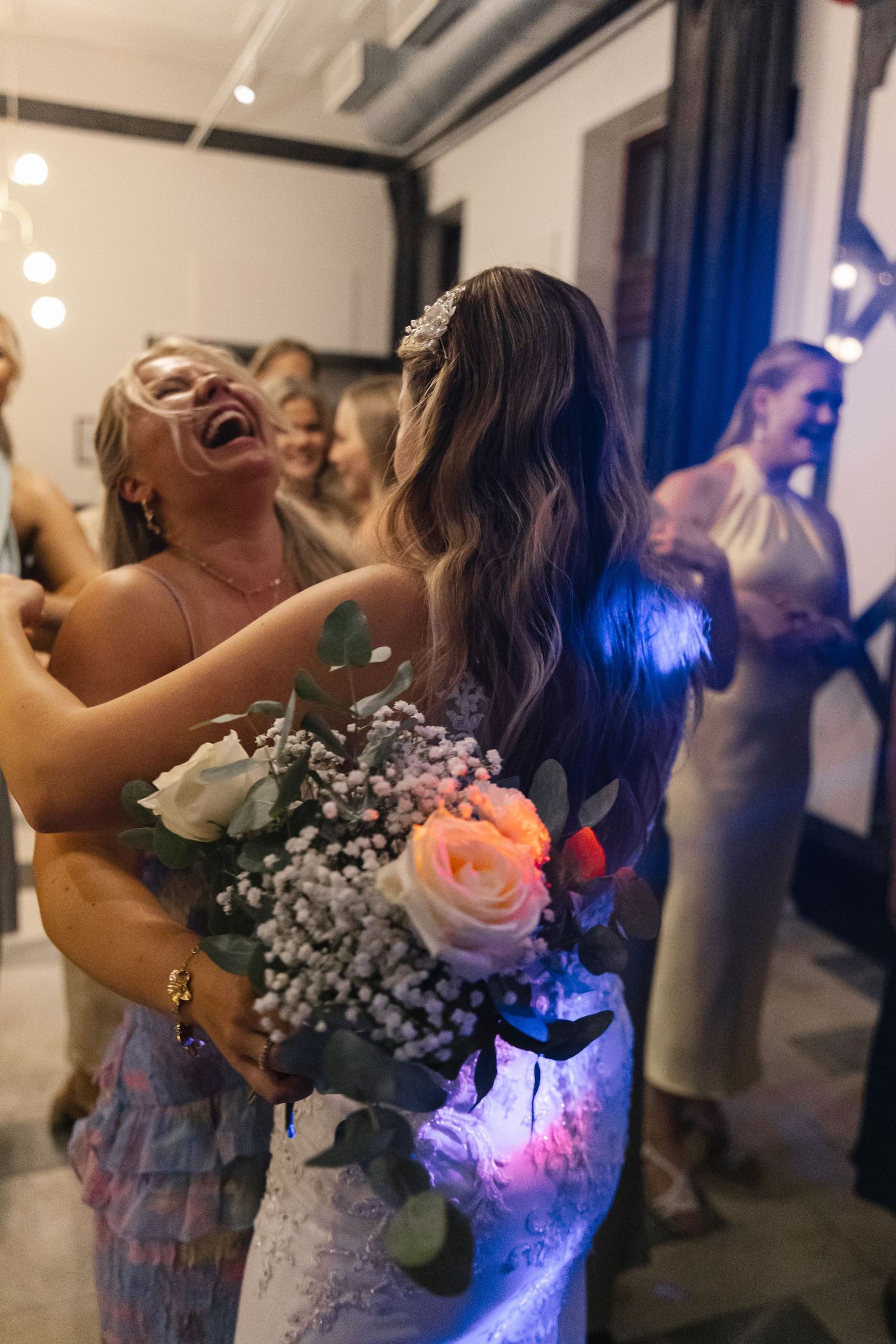 Wedding celebration with dancing and bouquet in hand under blue lighting.