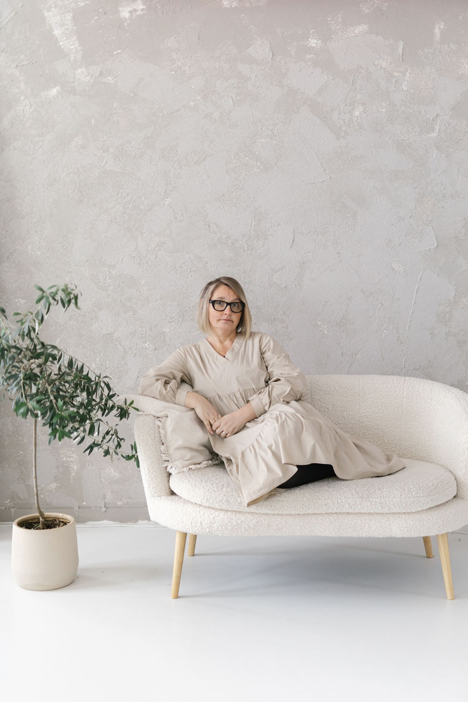 Minimalist white sofa with wooden legs against concrete wall with decorative potted plant in modern interior setting.
