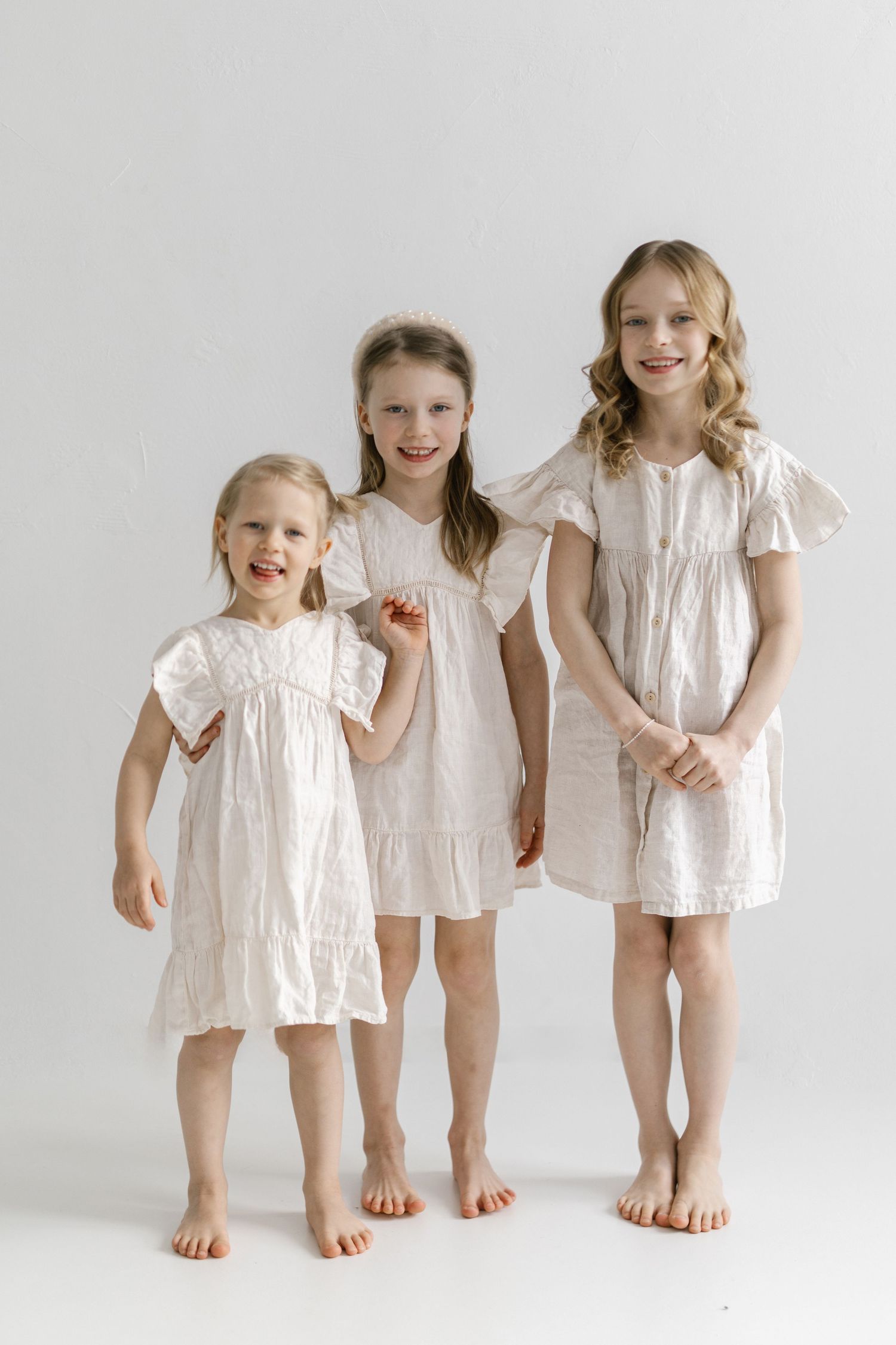 A series of five photos showing children in white dresses standing against a light background.