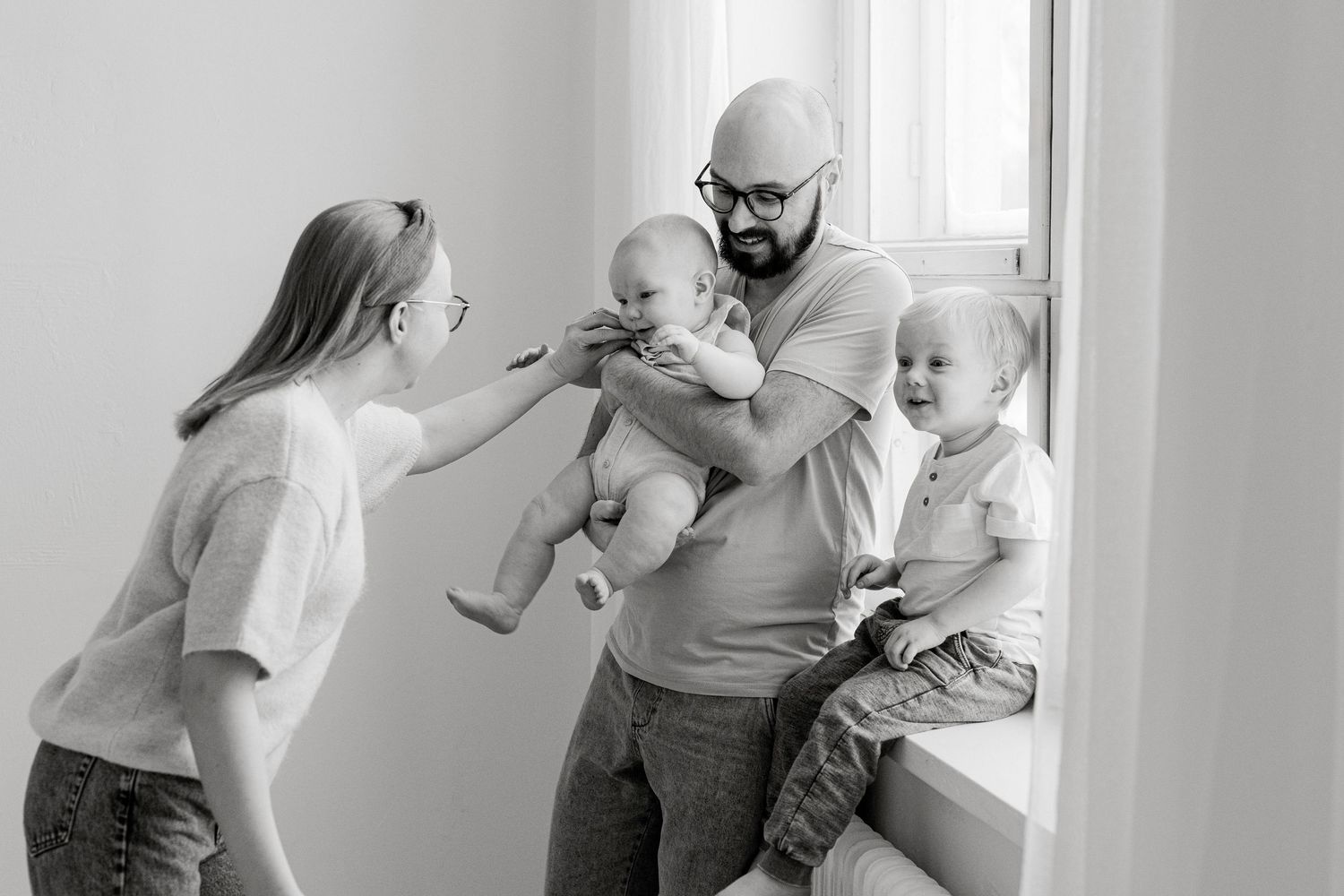 Black and white candid family moment showing playful interaction near a window.