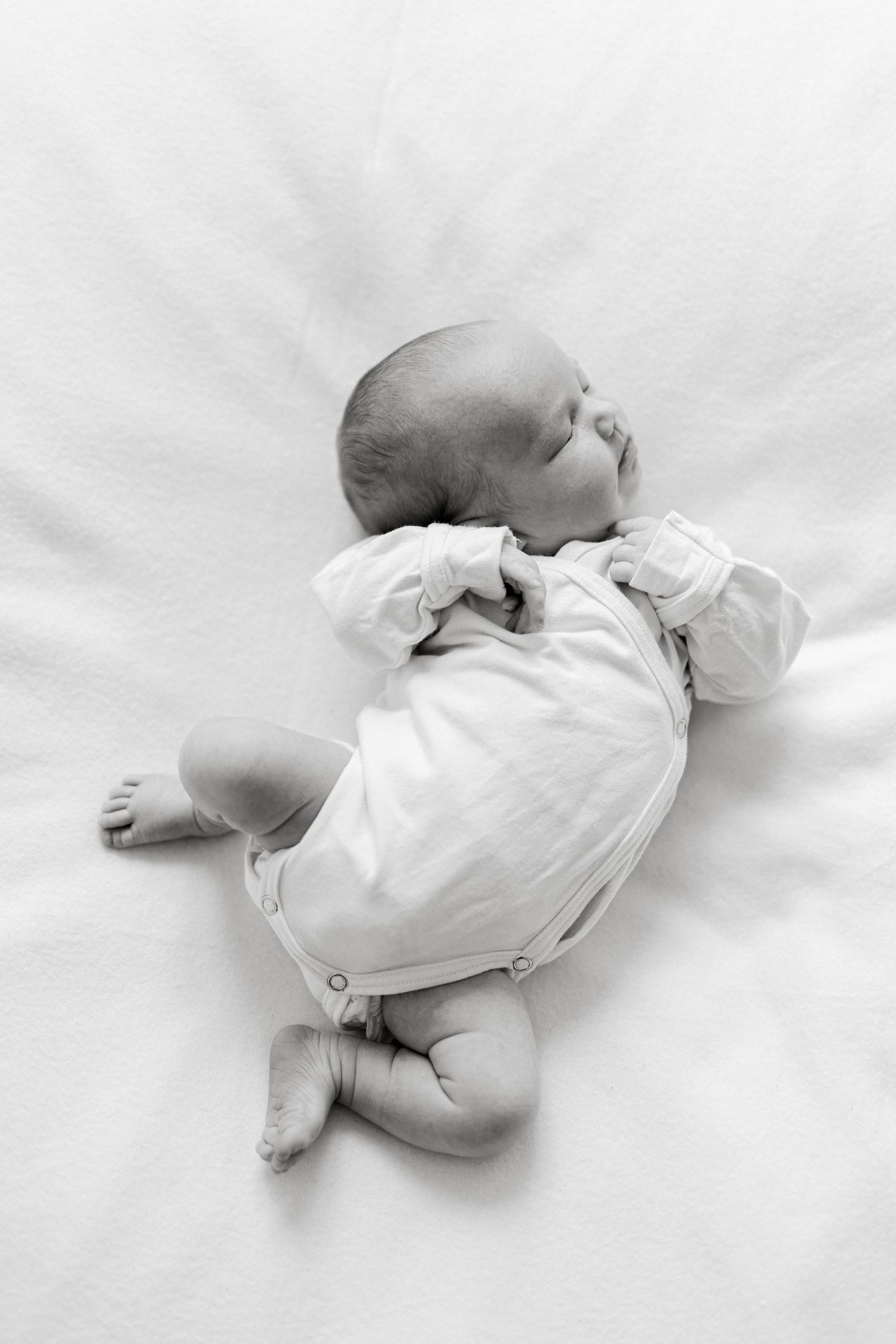 Black and white portrait of sleeping newborn in white onesie on light background.