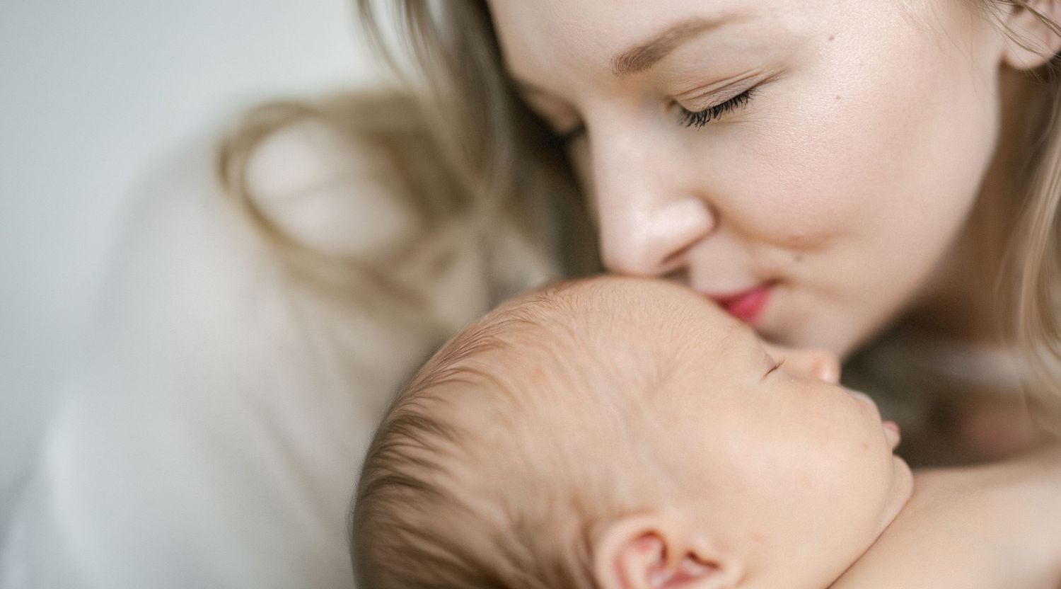 A tender mother gently nuzzles her sleeping newborn baby, capturing a serene and loving bond.