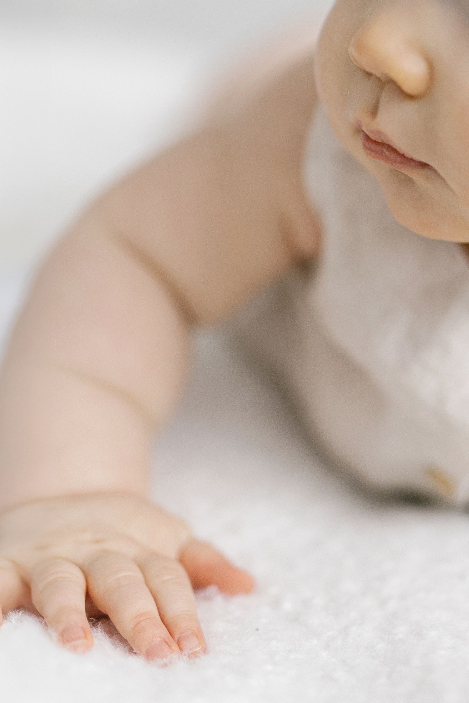 Close-up of a baby lying on a soft white blanket, reaching out with tiny fingers.