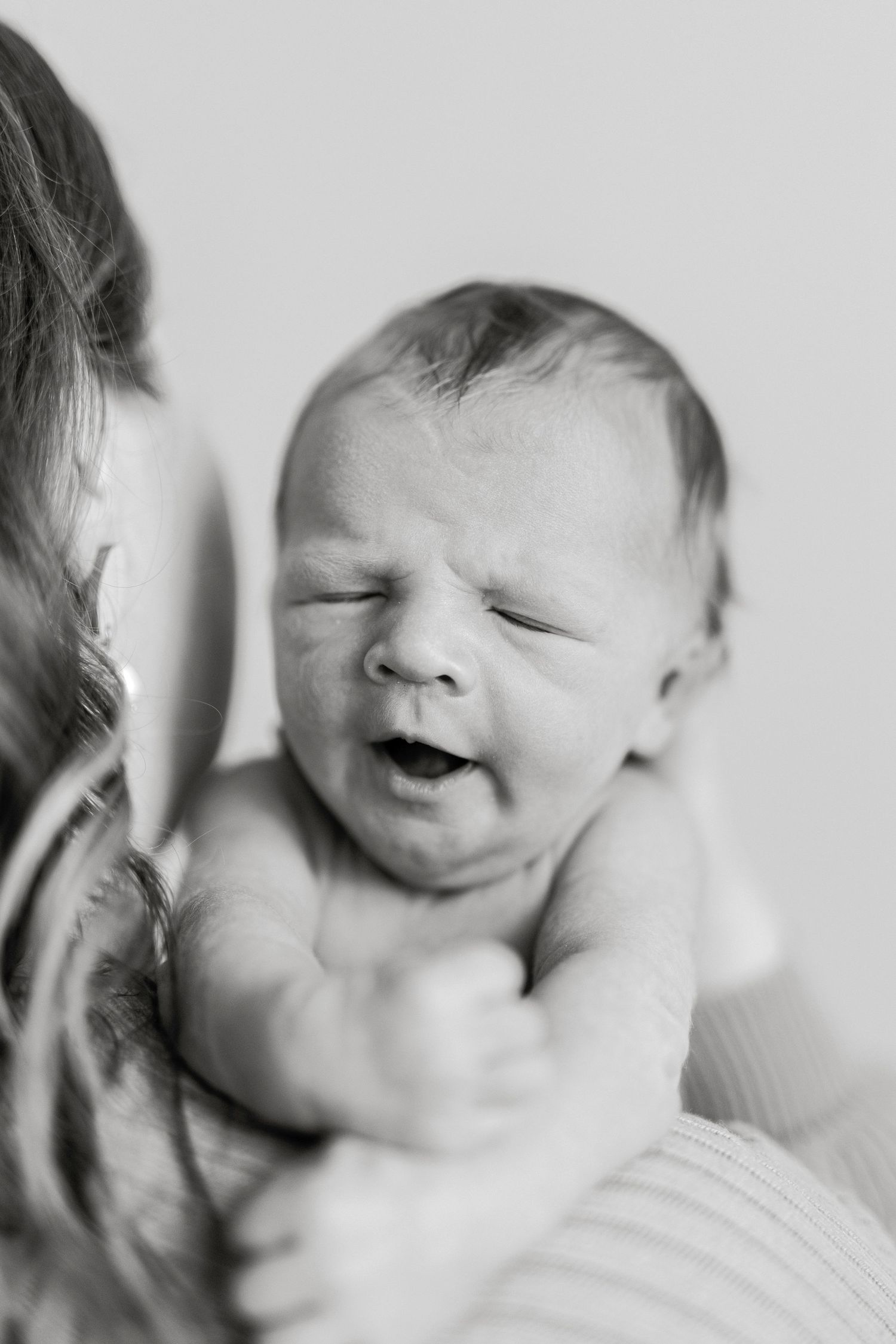 Black and white photo of a newborn baby making a funny face while being held by their mother.