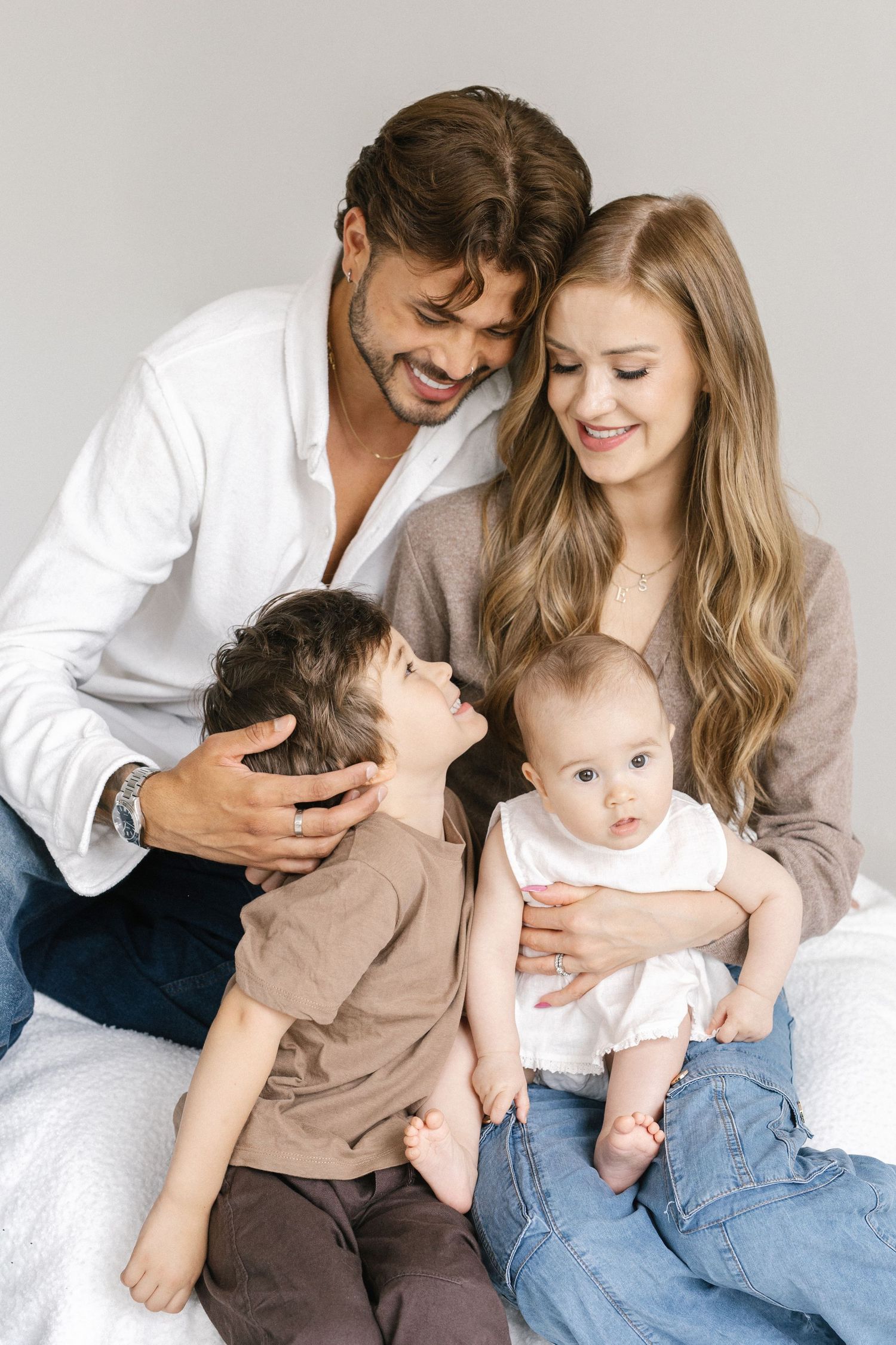Happy young family with toddler son and baby daughter posing together for a portrait on a white background.