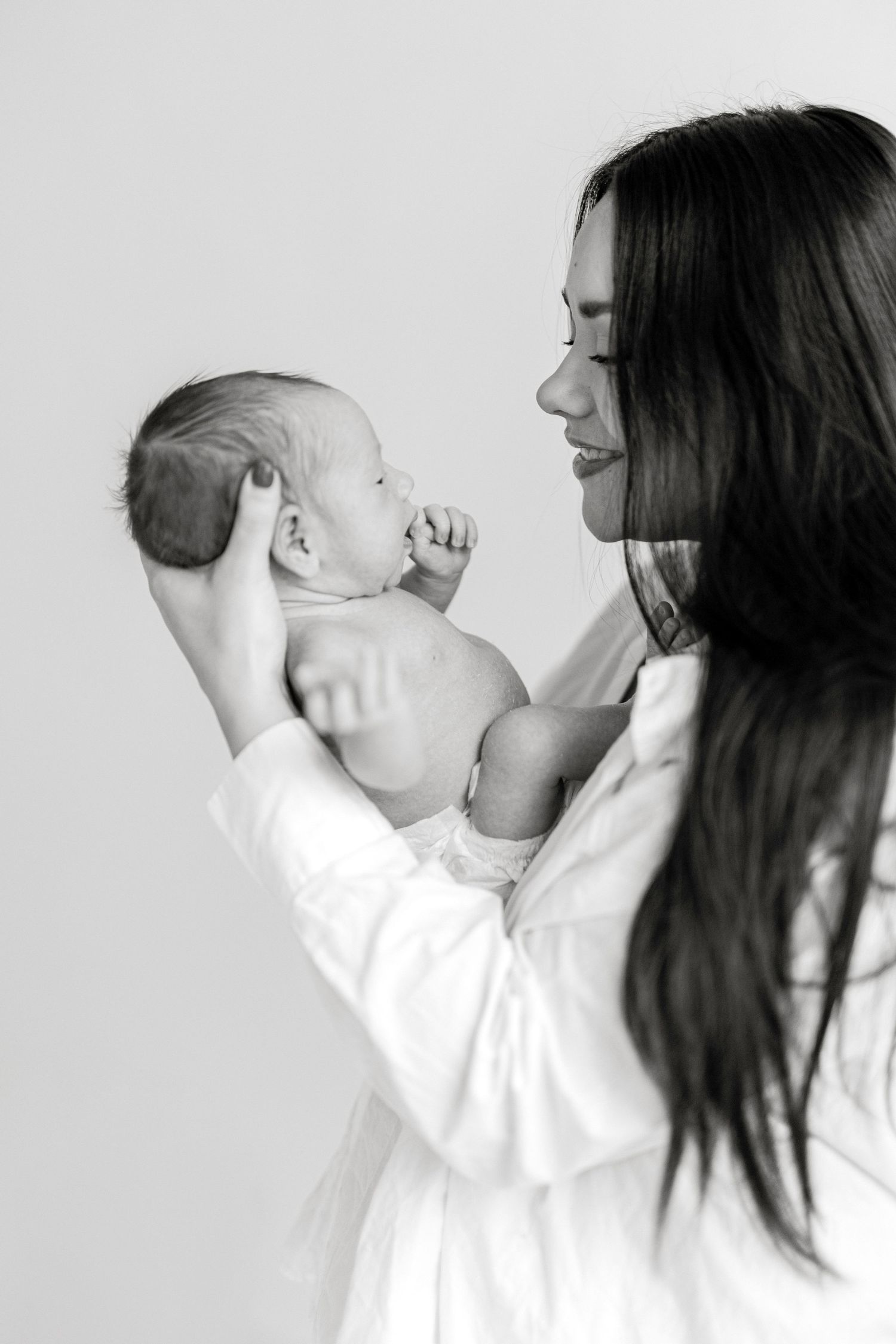 Mother in white holding newborn baby against minimalist background.