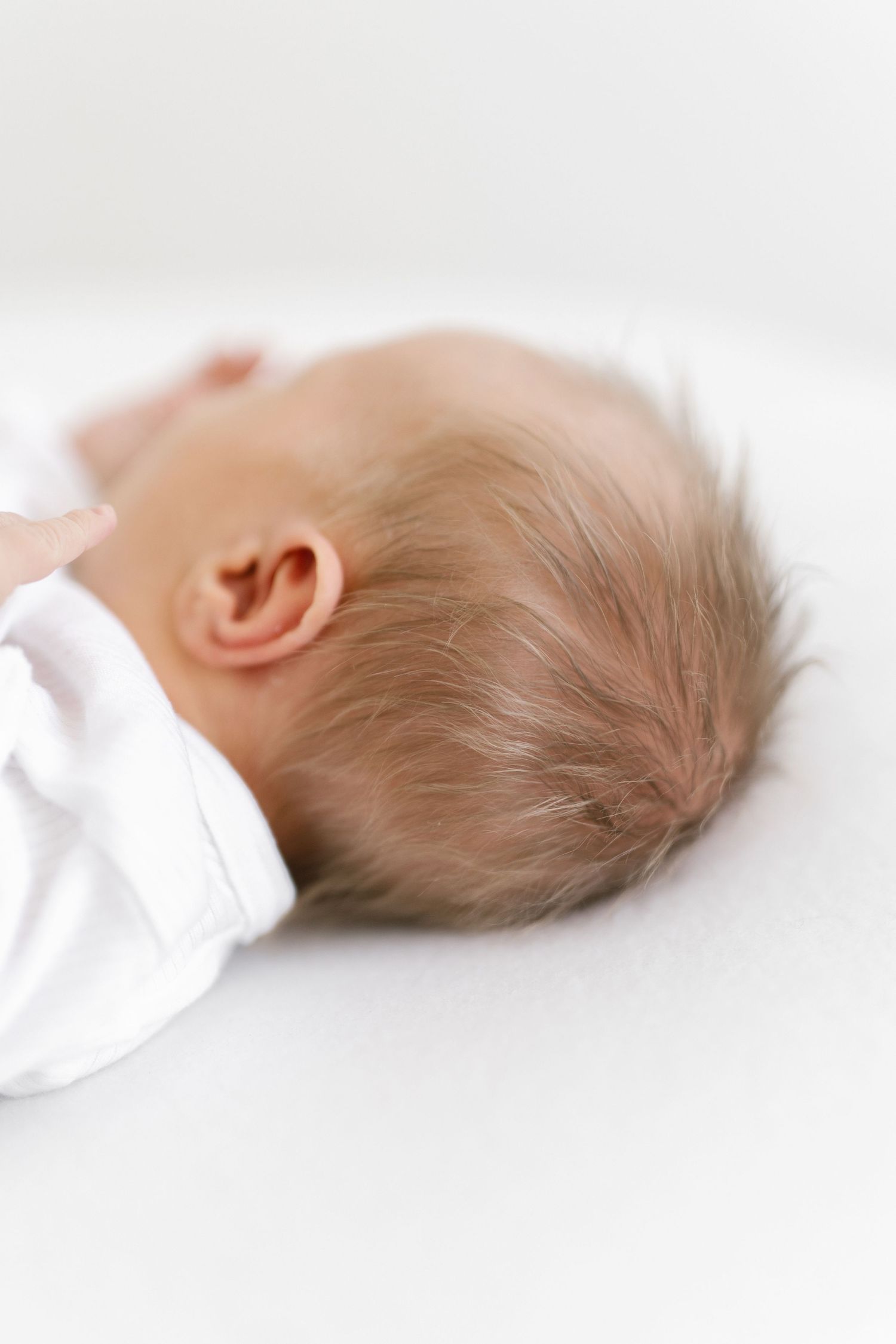 Minimalist side view of sleeping newborn baby in white against light background.