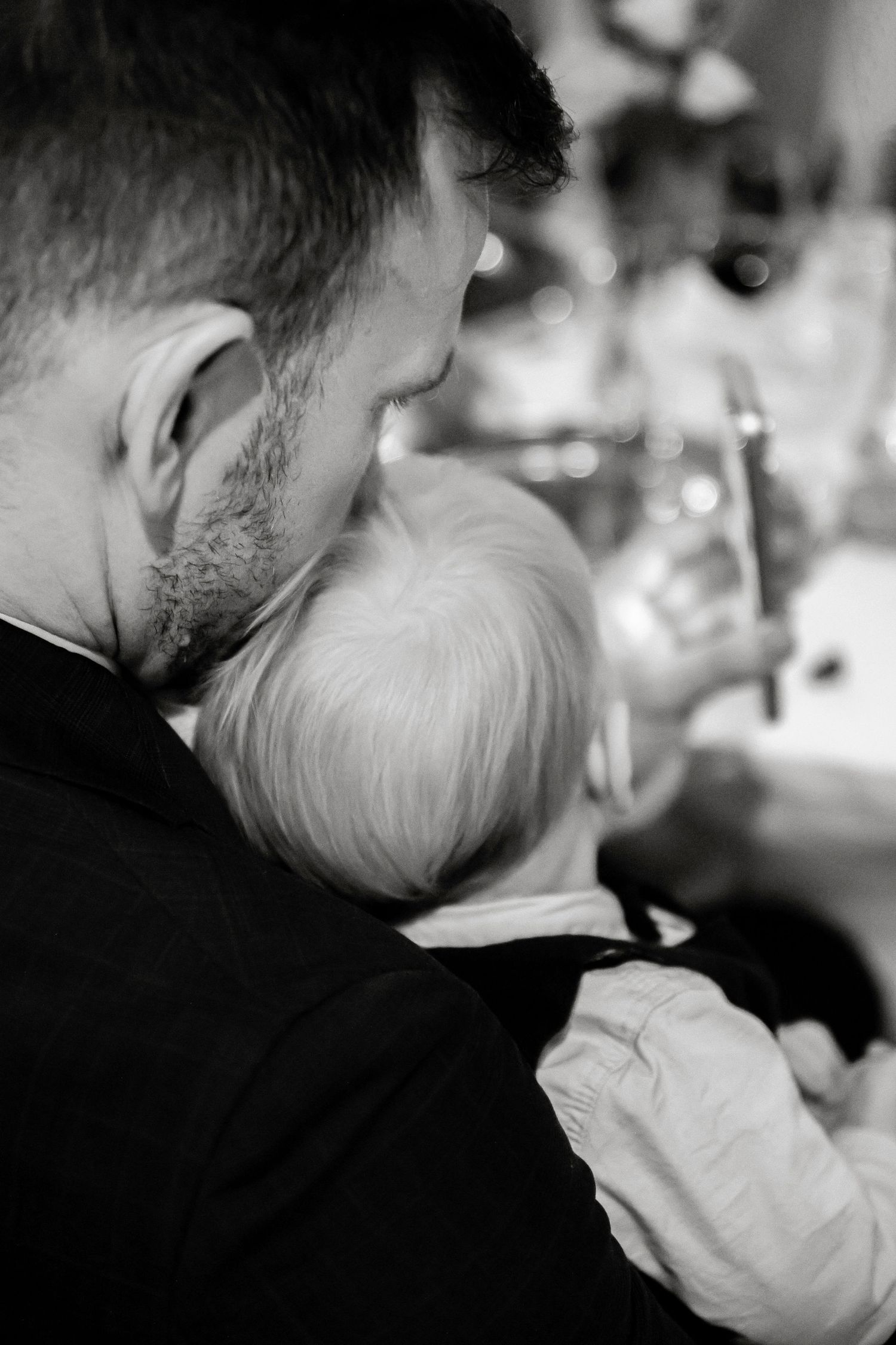 Father tenderly holds young child in black and white wedding reception photo.