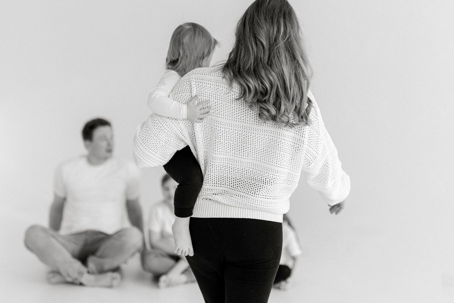 Black and white photo of a family playing together in a minimalist white studio setting.