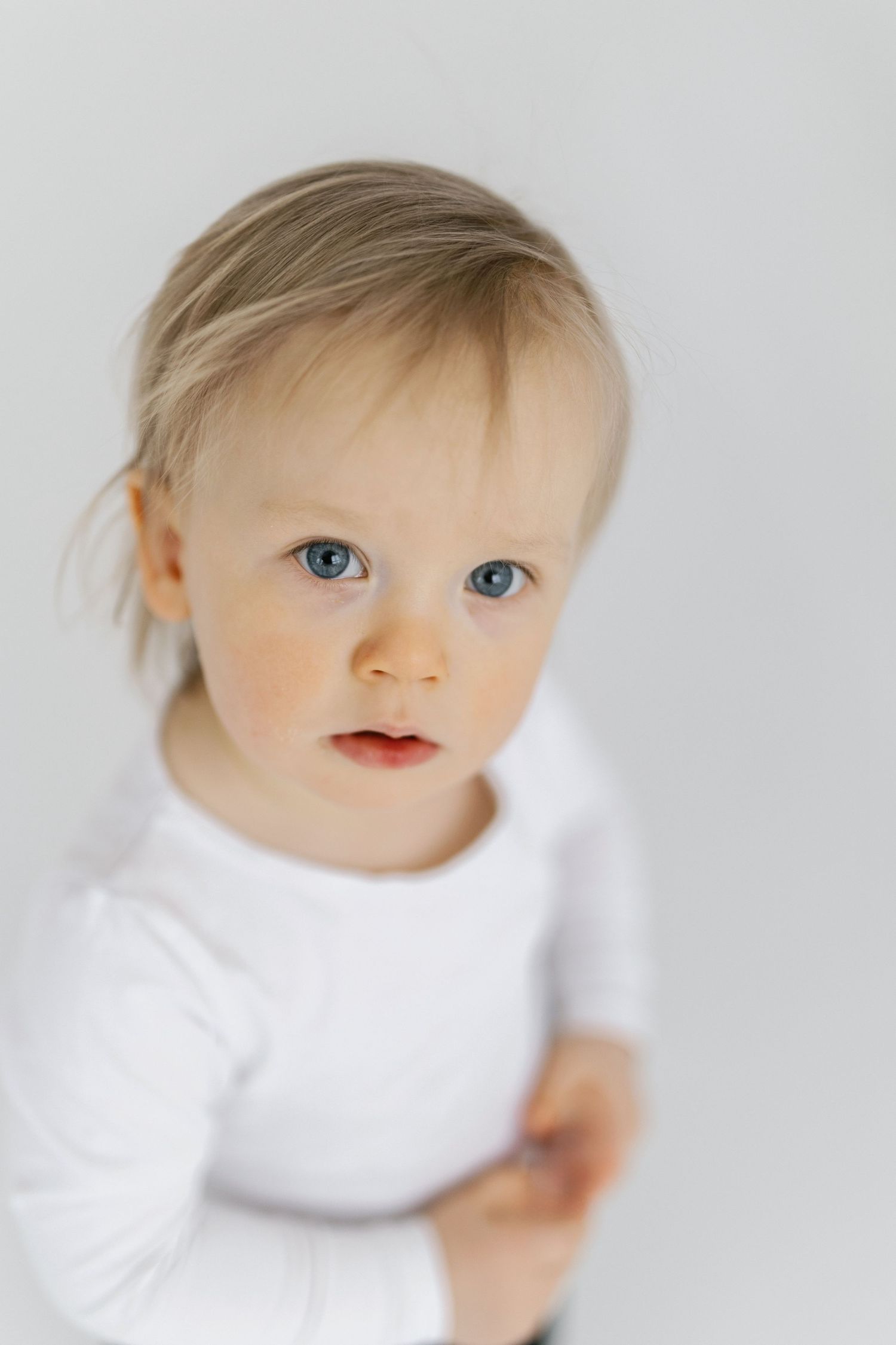 A baby in a white shirt looks off to the side with bright blue eyes in a series of soft focus portraits.