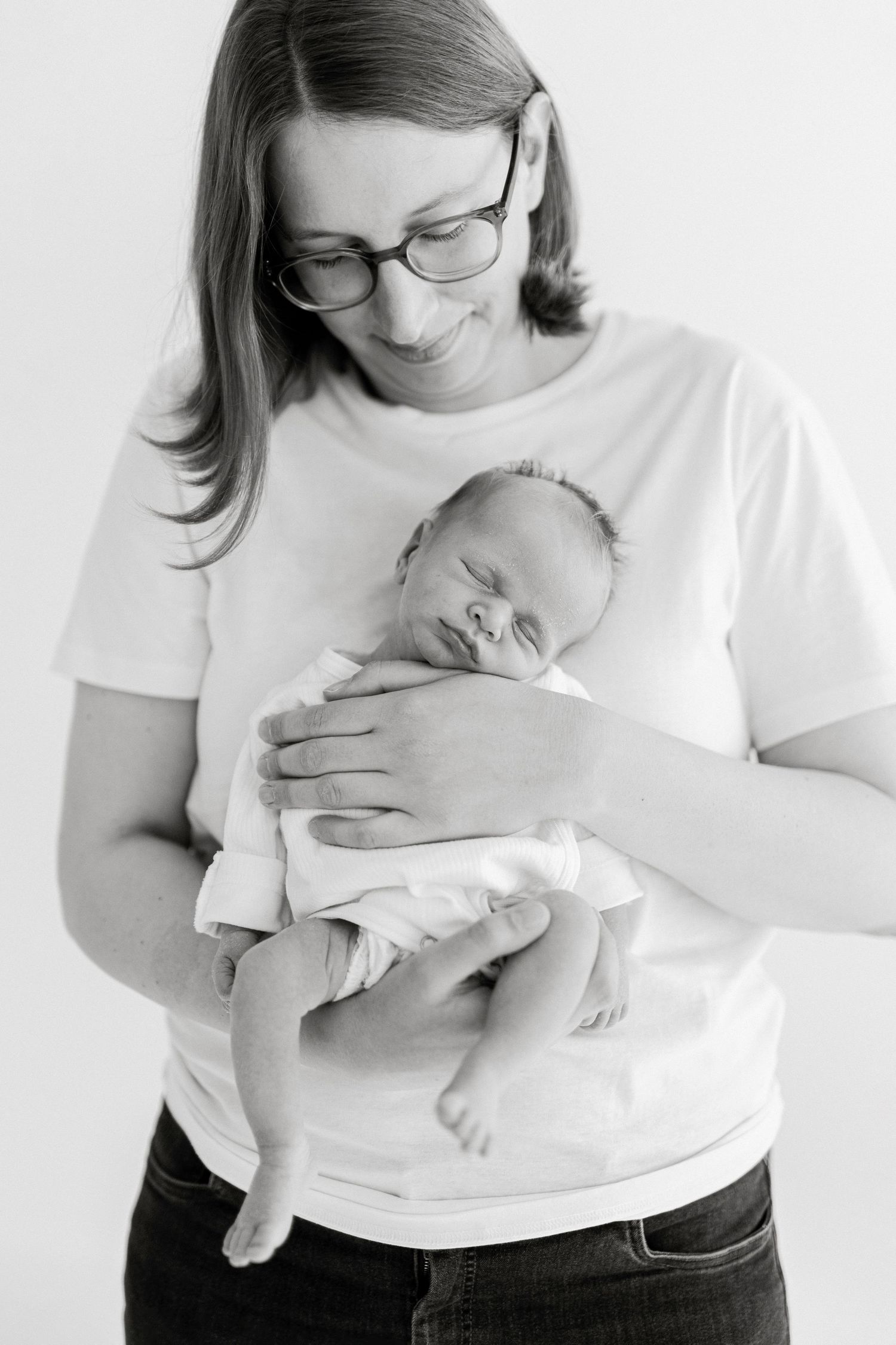 Parent in glasses and white shirt holding newborn baby in intimate portrait series.
