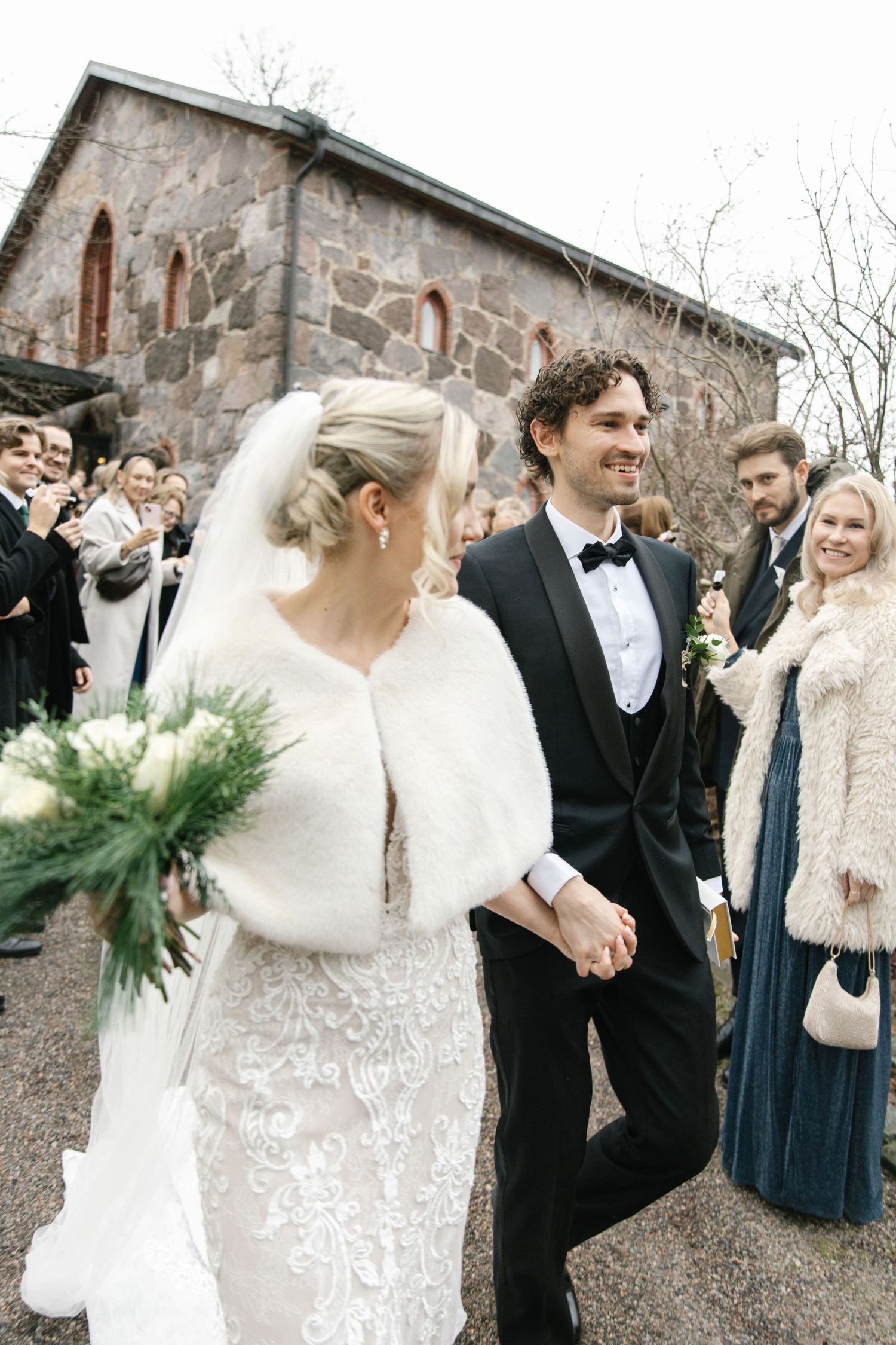 Joyful wedding celebration outside historic stone church with guests in formal attire.