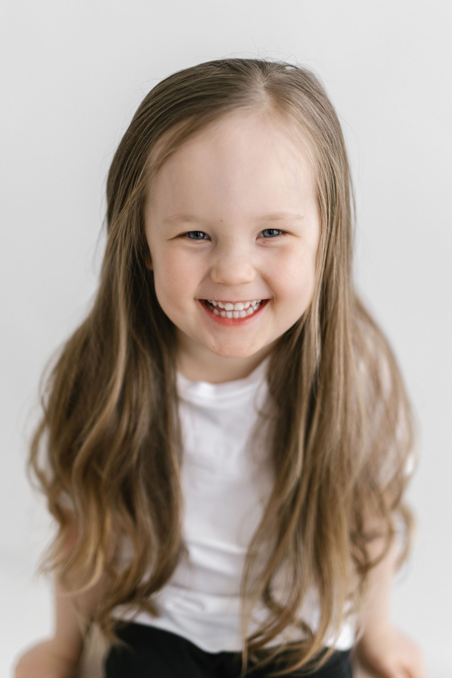 A series of five photos showing a child with brown hair in a white shirt expressing different joyful emotions.