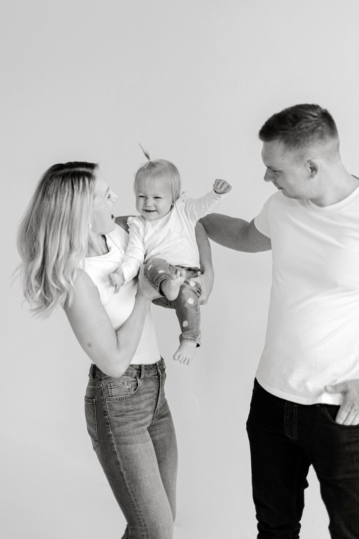 Black and white photo of happy young family with mother holding smiling baby while father reaches out to touch child.