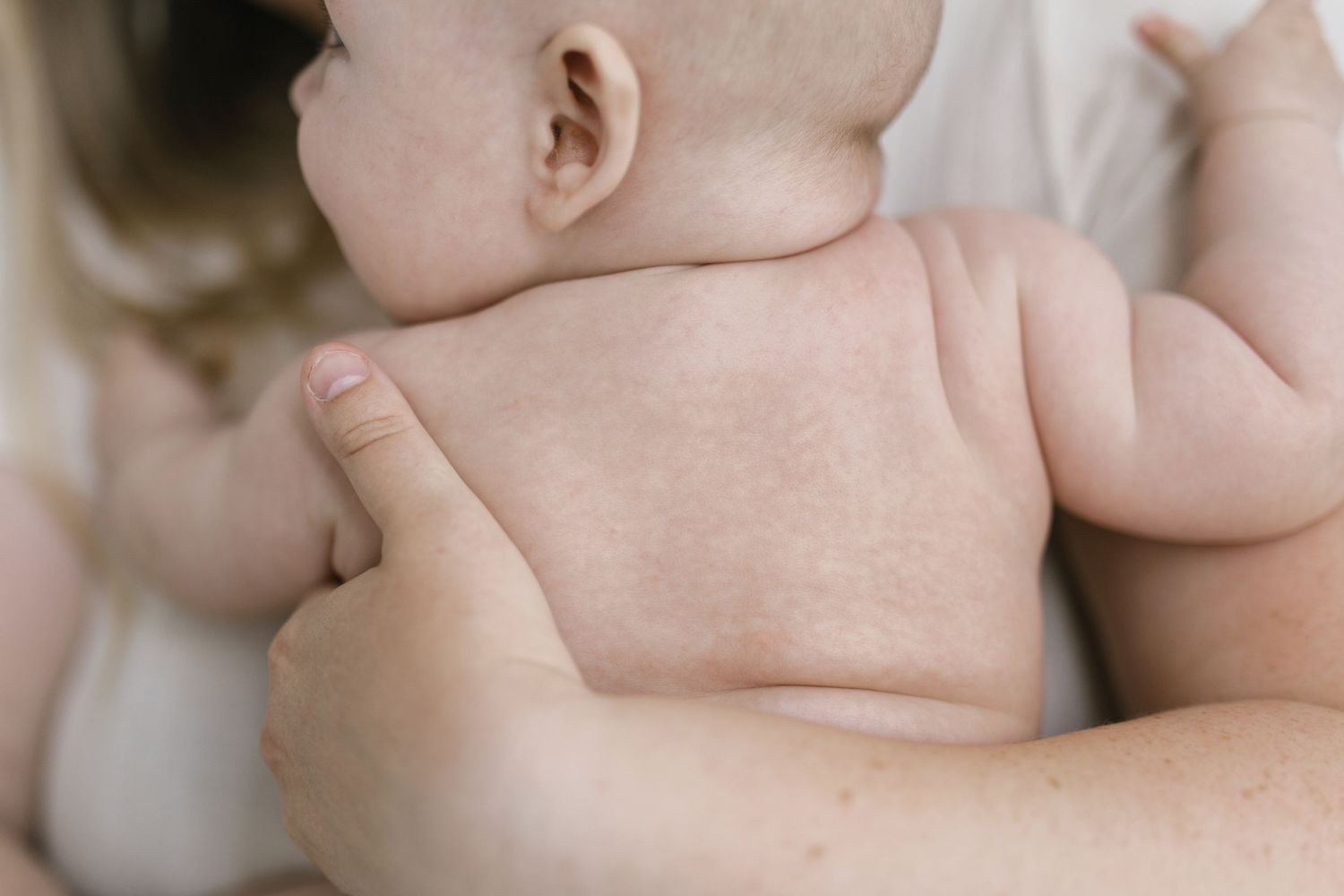 Close-up of a newborn baby being held against an adult's chest, showing the infant's soft skin and tiny back.
