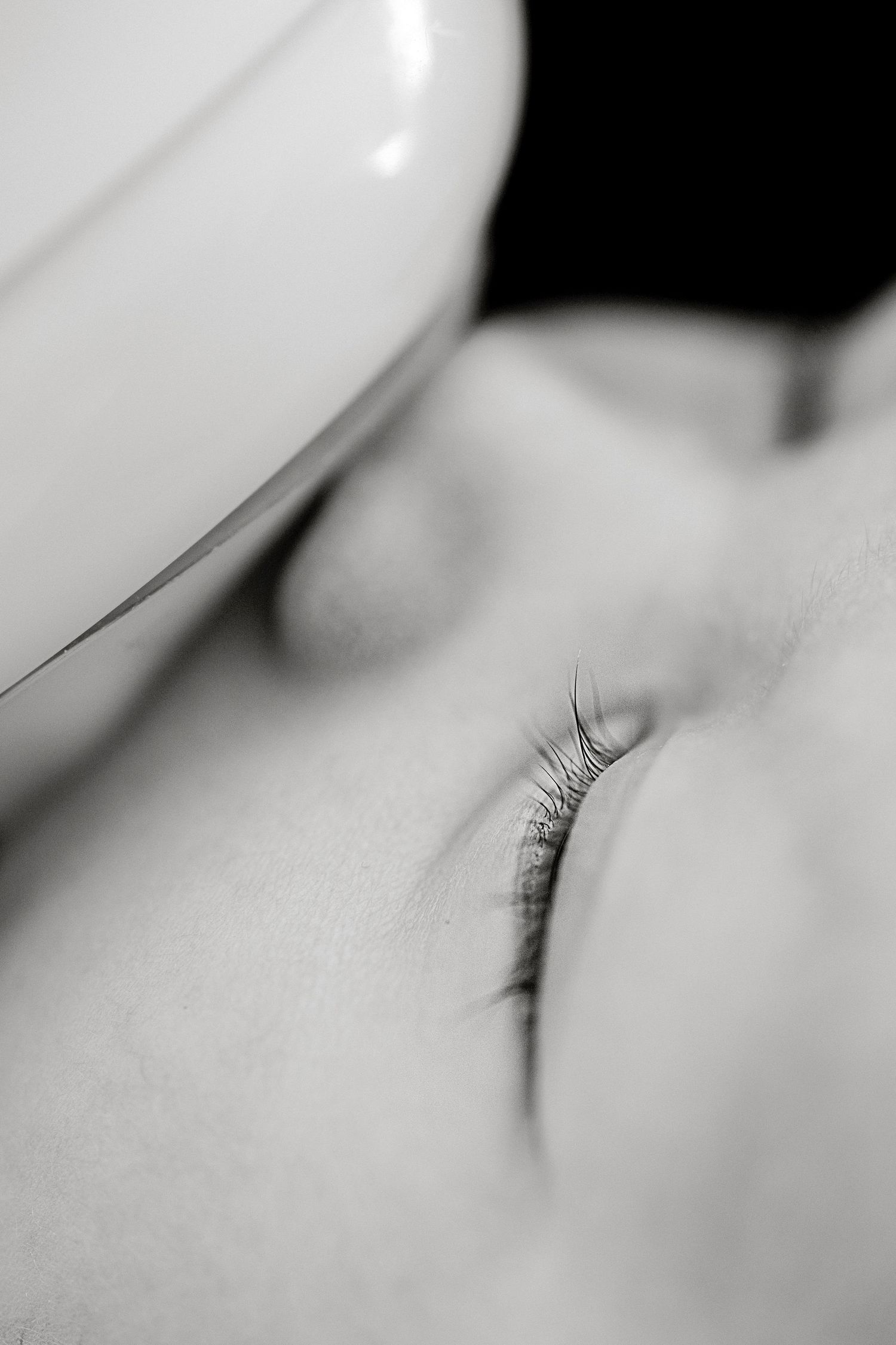 Close-up black and white photo of a sleeping baby with delicate eyelashes, peaceful expression, soft skin texture.