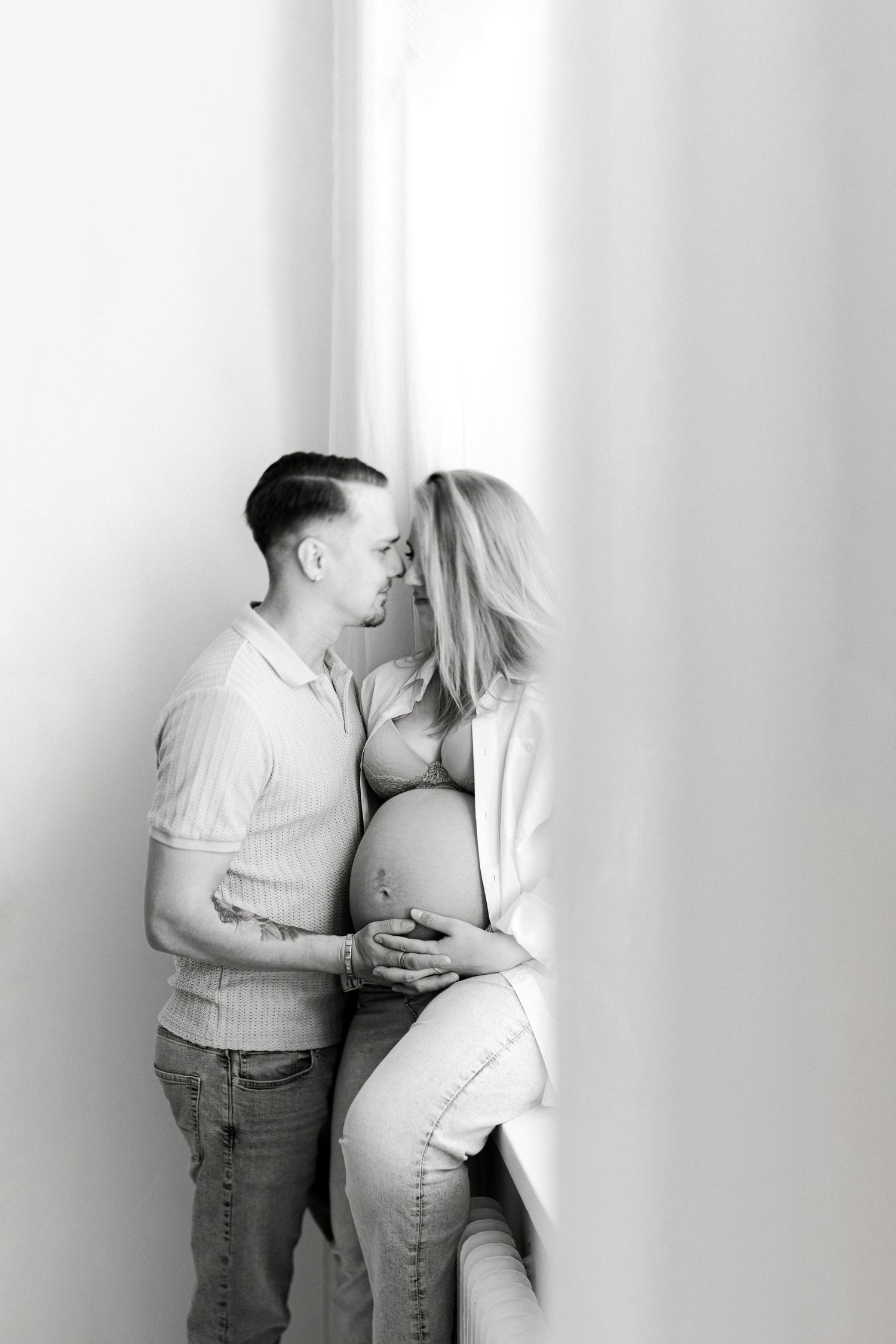 Black and white maternity photo of a couple embracing and sharing a tender moment while cradling a pregnant belly.
