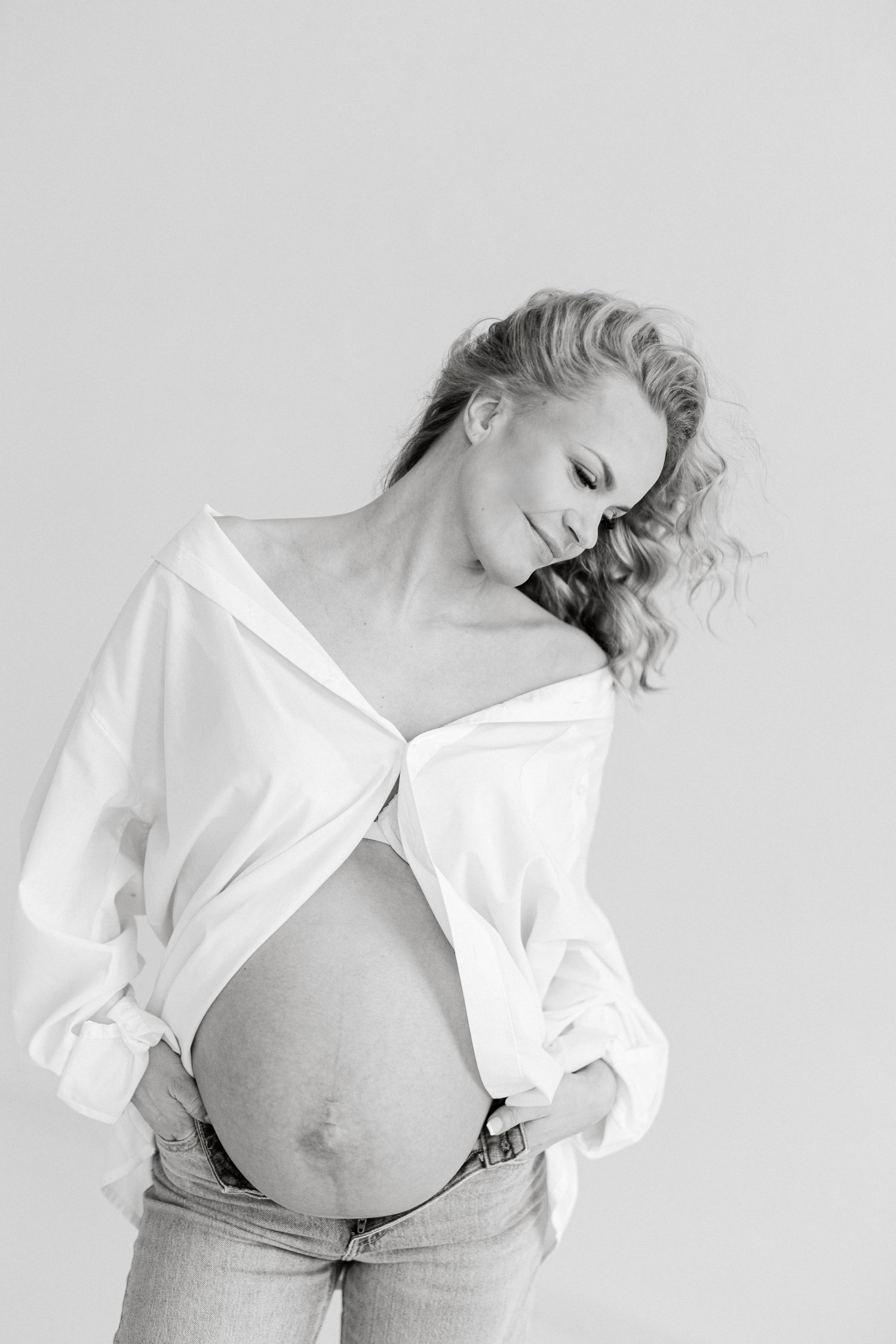 Black and white artistic maternity portrait with white shirt and denim in natural light.
