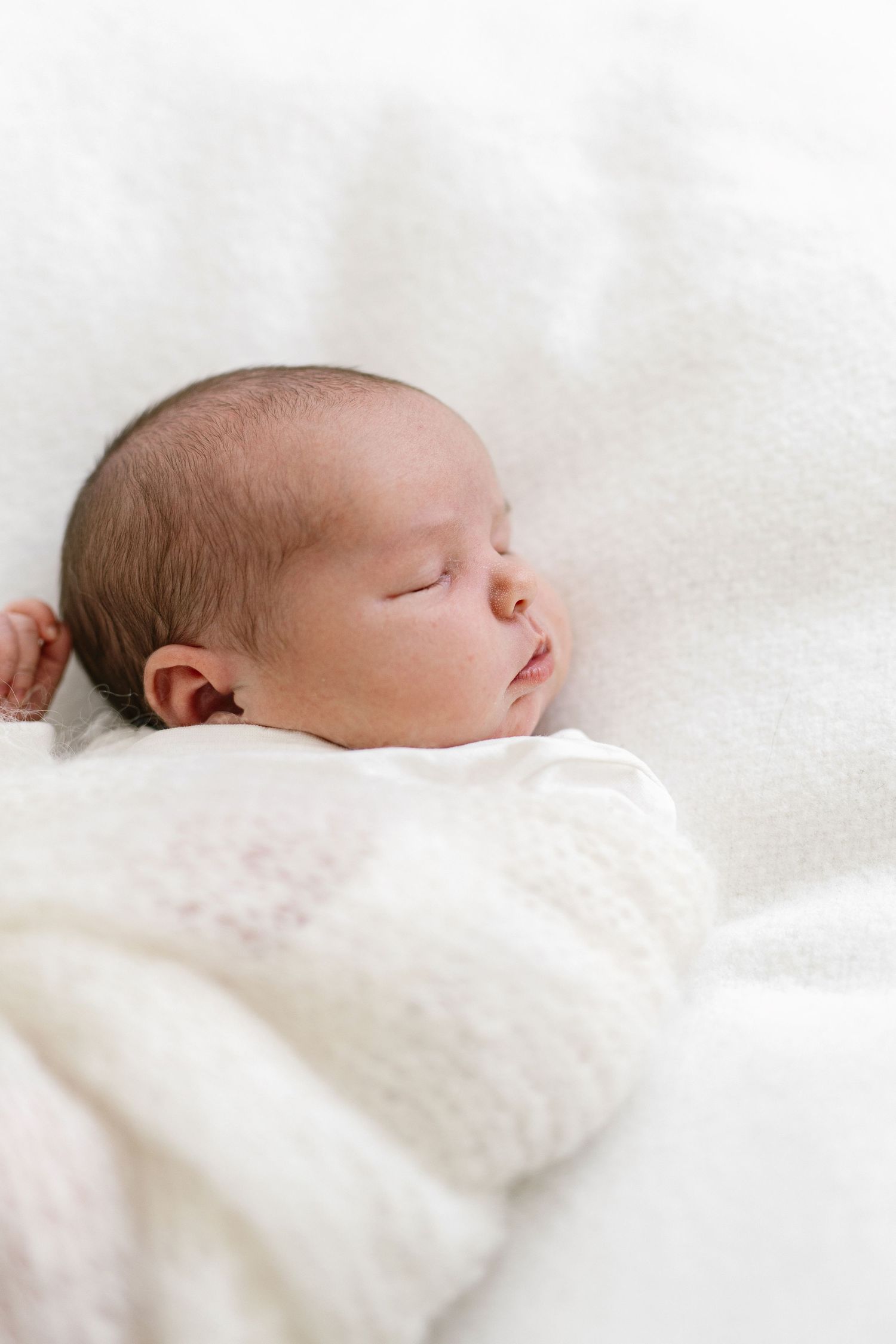 Peaceful newborn baby sleeping soundly wrapped in soft white knit blanket, perfect newborn photography portrait.