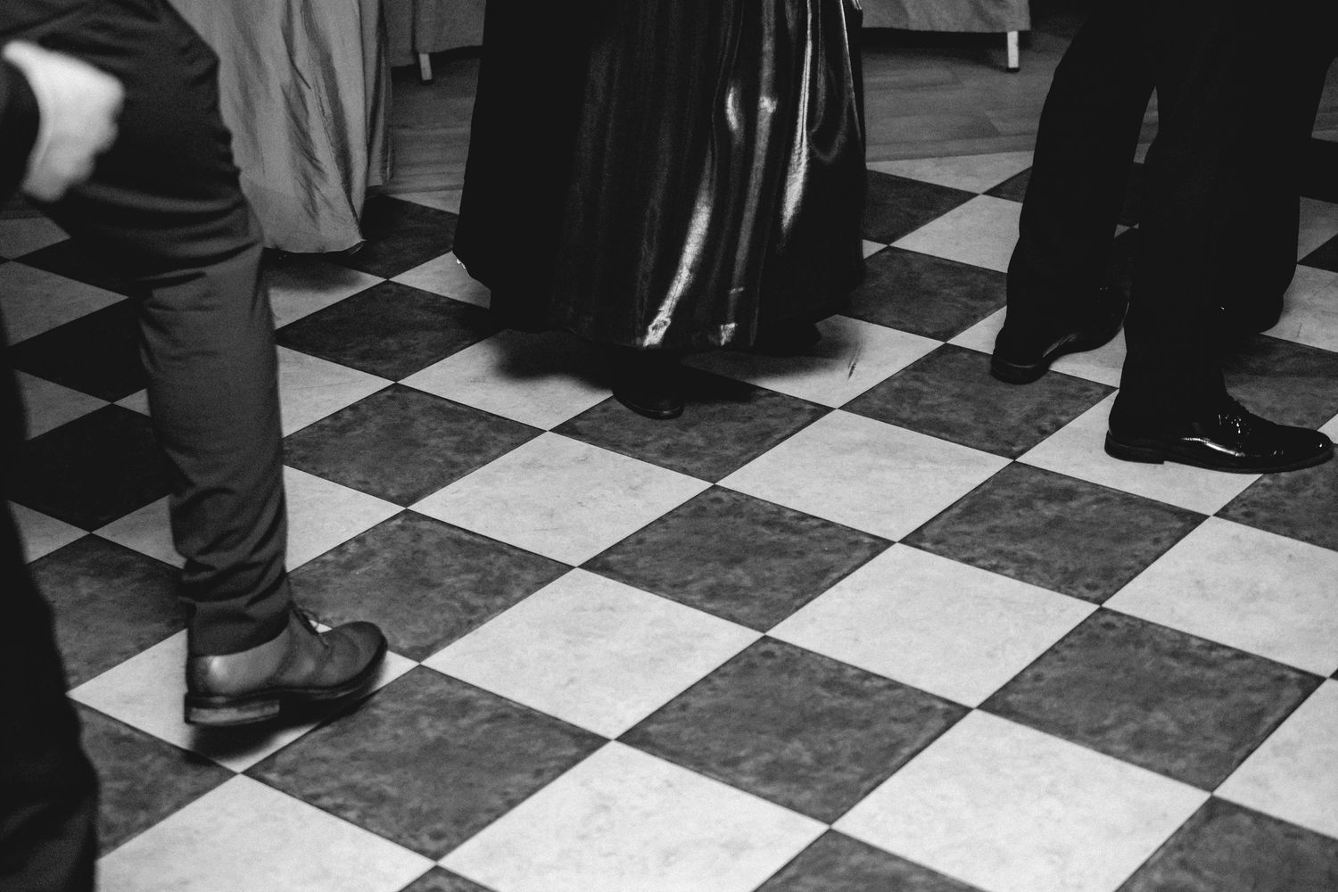 Black and white photo of wedding guests dancing on checkered floor.