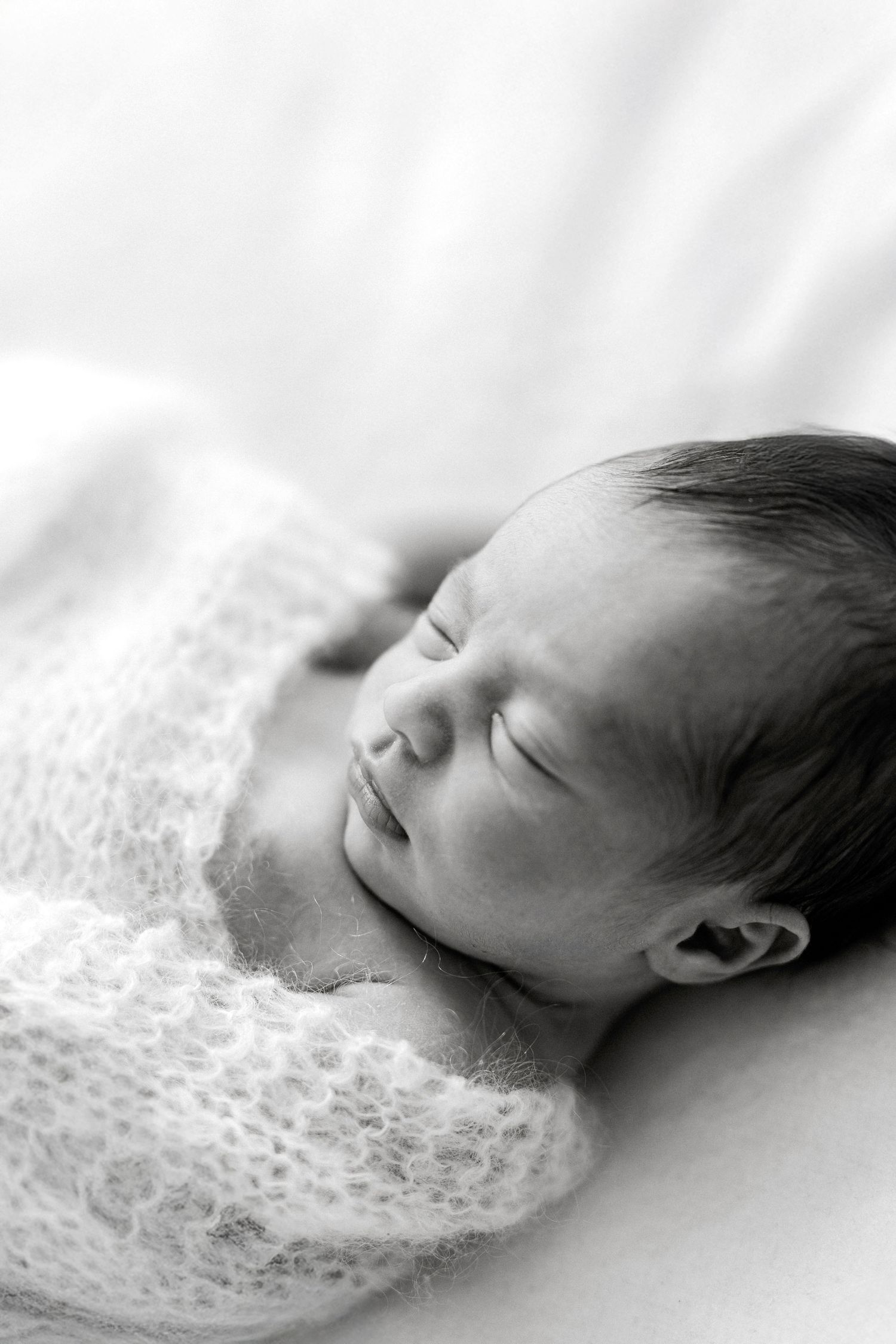 Black and white photo of a peaceful sleeping newborn baby wrapped in a soft knit blanket.