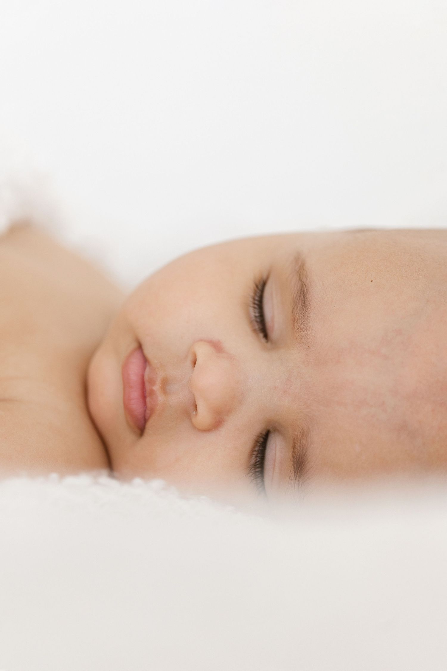 Close-up of a peaceful sleeping baby with soft skin resting on a white fluffy surface.