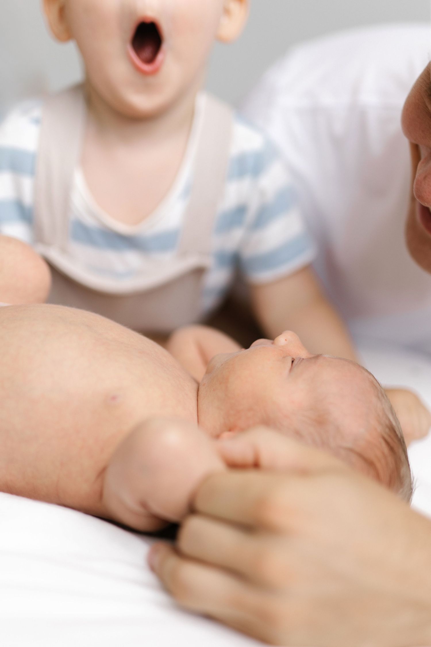 Close-up of a sleeping newborn while another child shows excitement in the background.