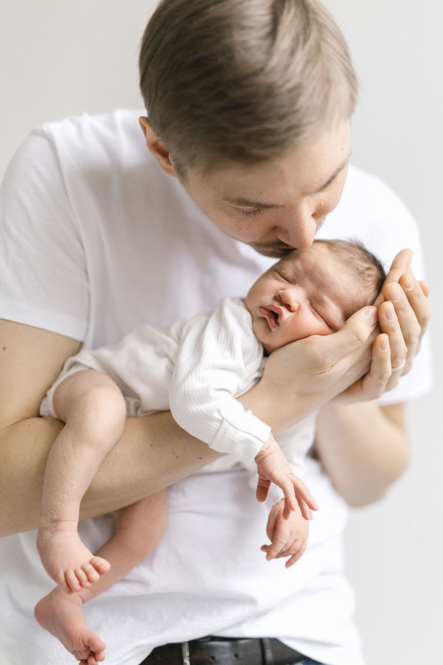 Parent in white shirt holding and kissing baby in tender sequence of loving moments.