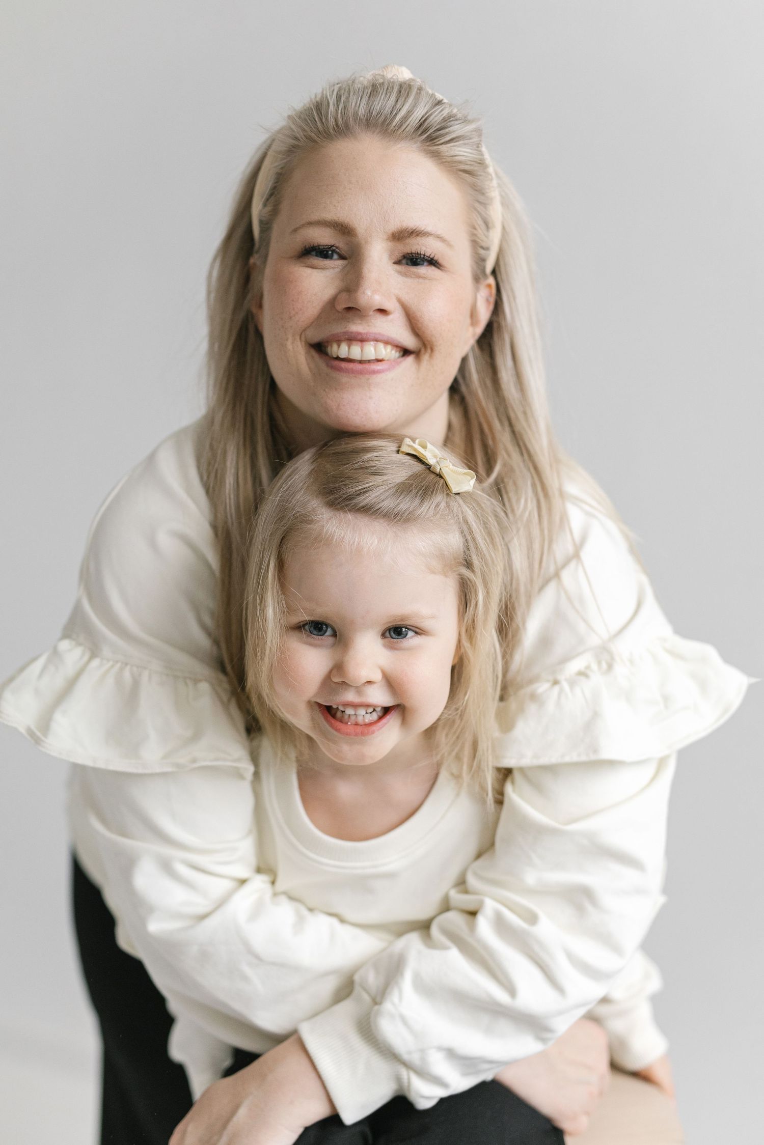 A heartwarming portrait of a mother and daughter in matching white tops sharing bright smiles.