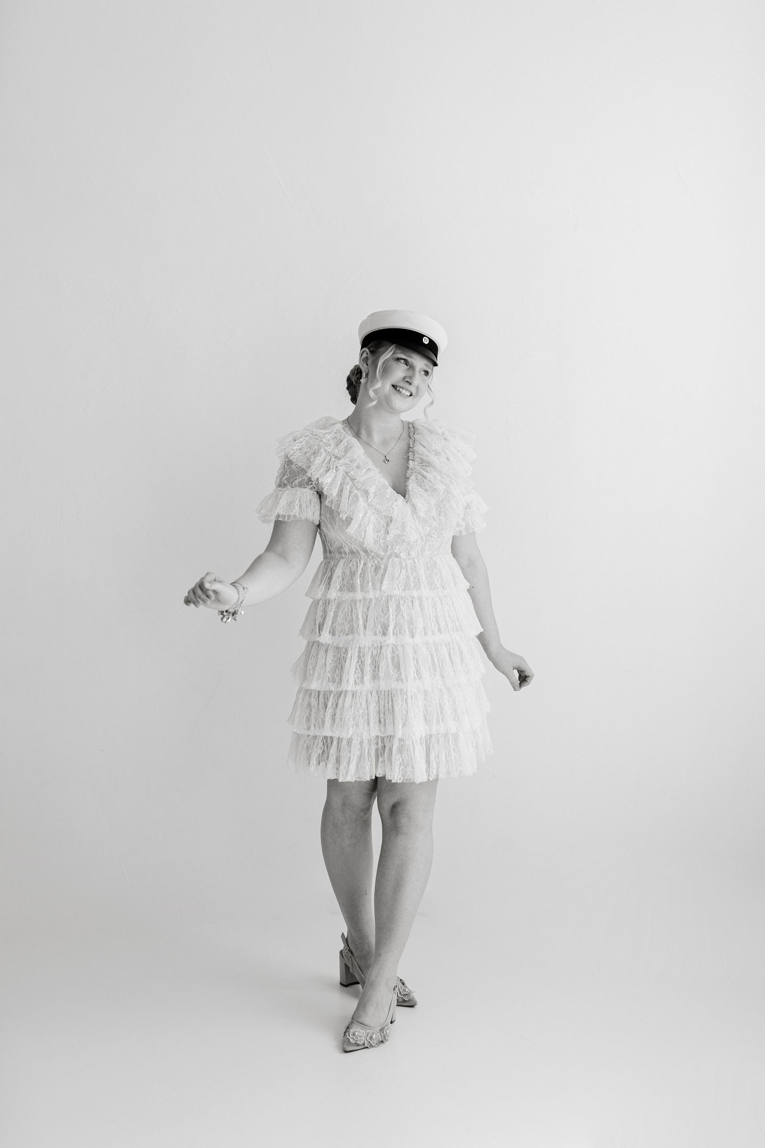 Black and white photo of a woman in a ruffled mini dress and cap, posing gracefully in a studio setting.