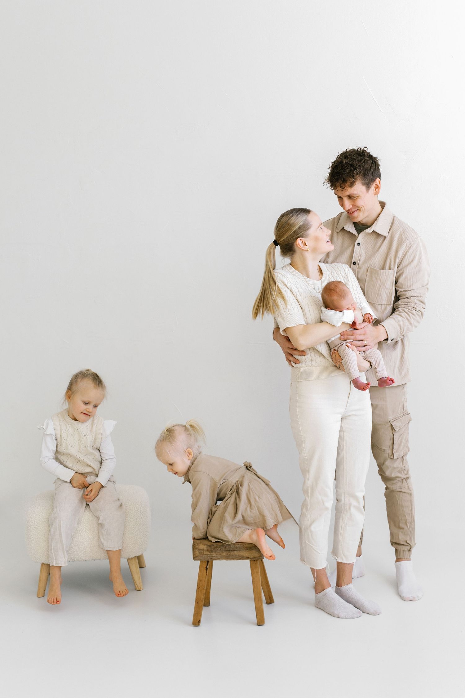 Happy family with newborn baby and two toddlers posing together in neutral tones against white background.