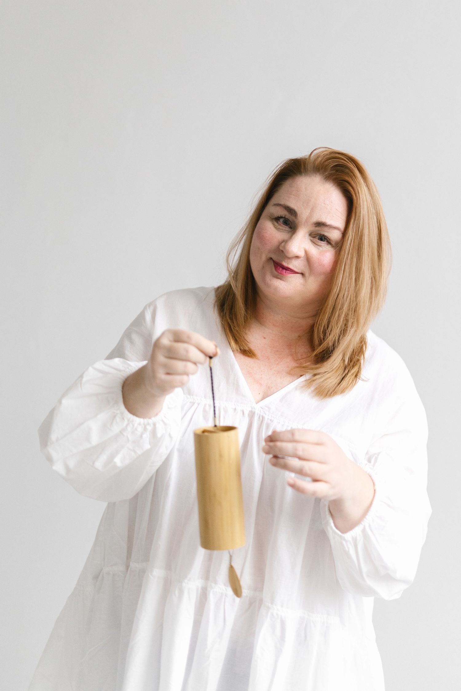 Woman in white dress smiling while holding a bamboo cup with string.