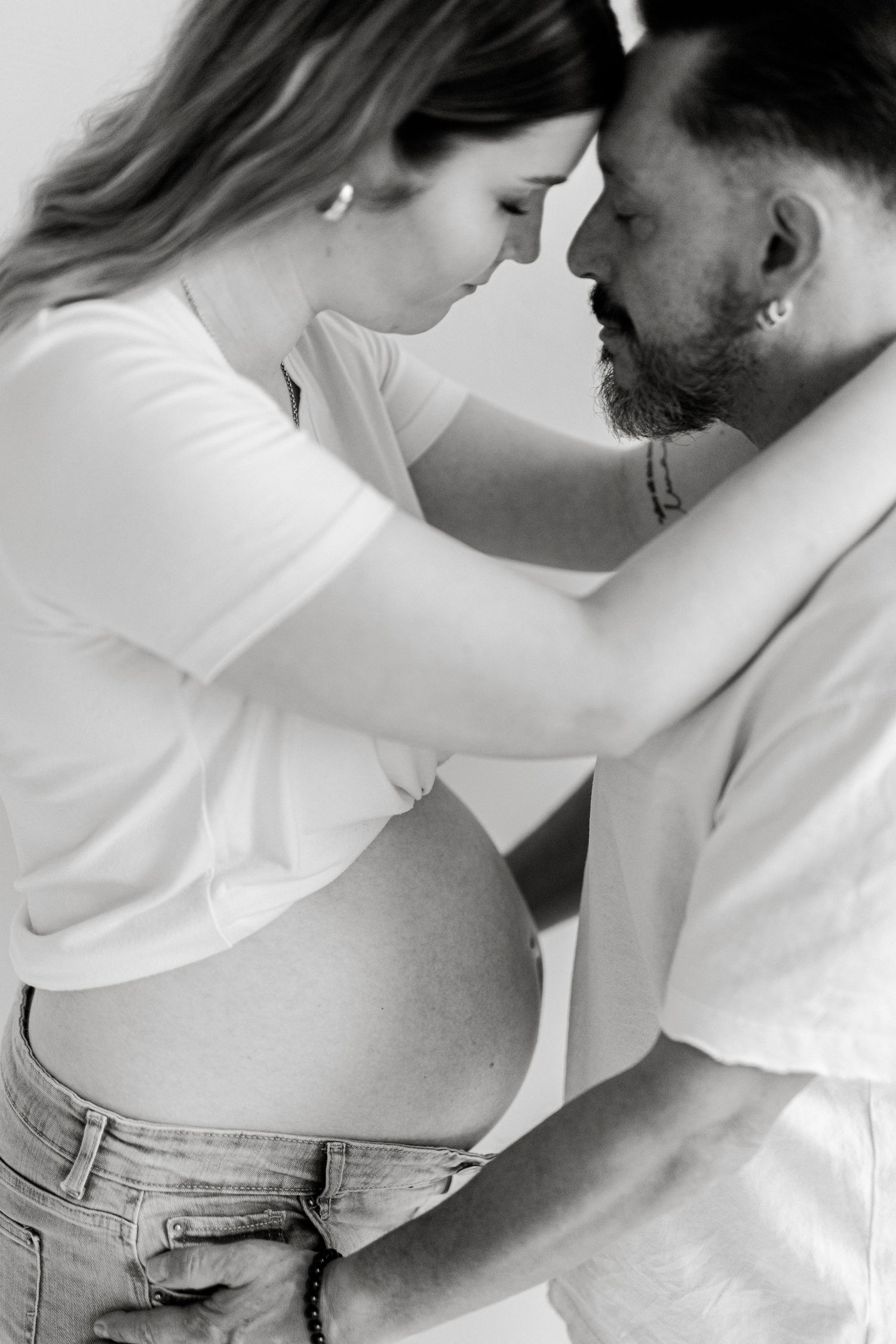 Black and white photo of a pregnant couple sharing an intimate moment, foreheads touching, celebrating their expecting journey.