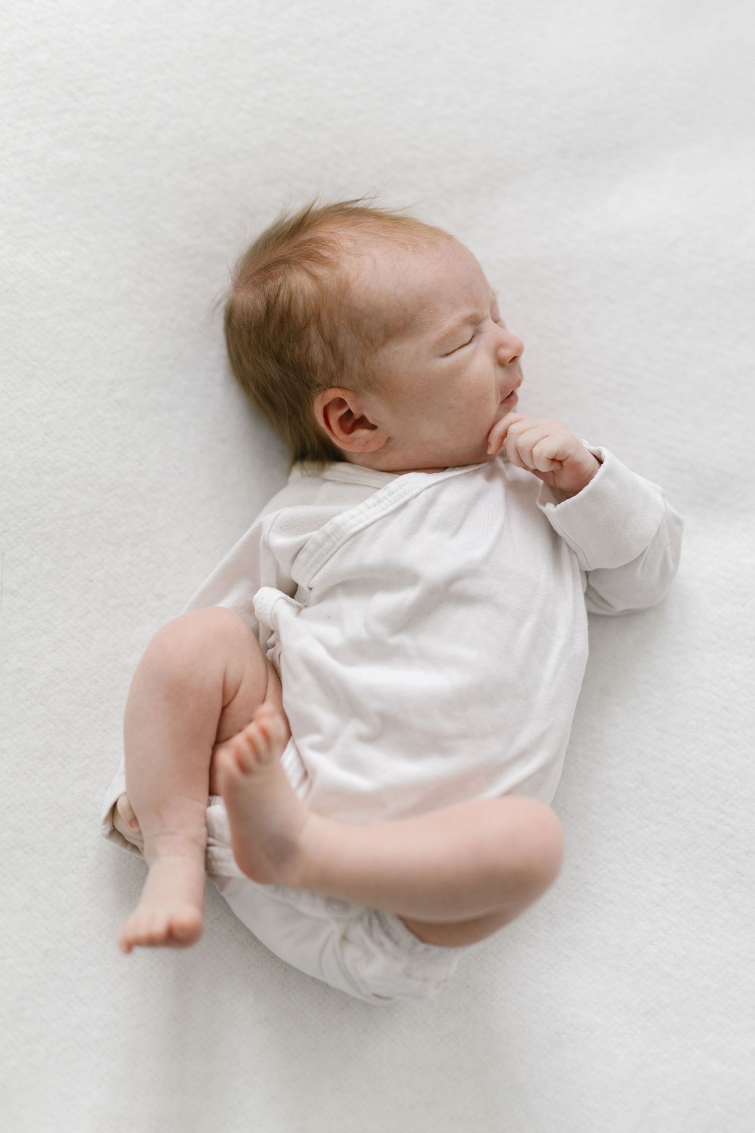 A sleeping baby in white clothing lies on a soft white surface in a series of peaceful poses.
