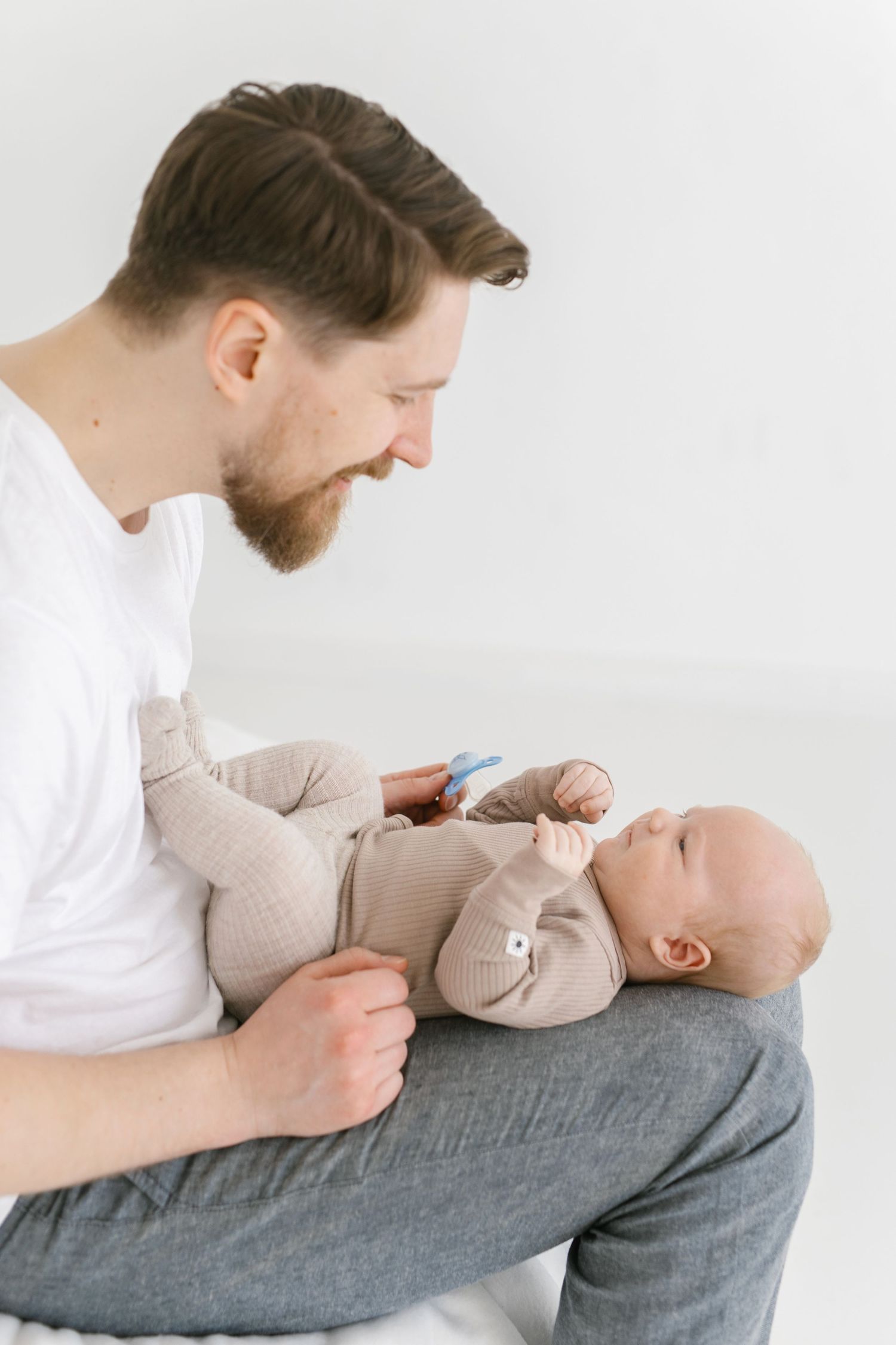 Smiling bearded father holding his newborn baby in a white studio setting.
