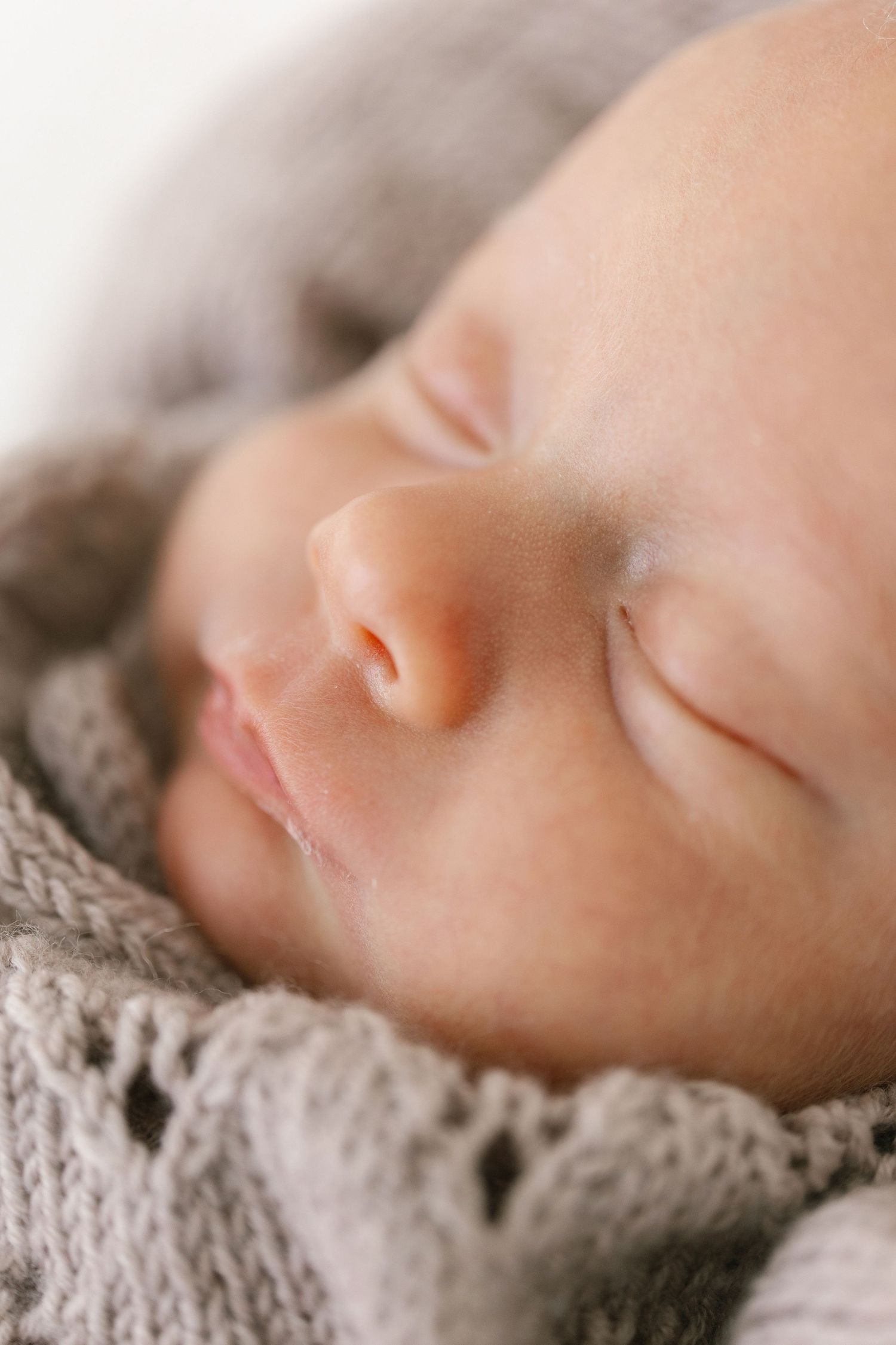 A peaceful newborn baby sleeping soundly, wrapped in a soft gray knit blanket, close-up portrait photography.