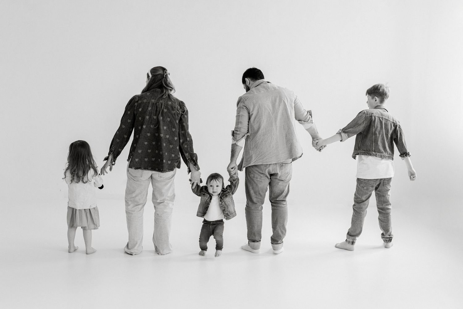 Black and white photo of a family of five walking together holding hands, viewed from behind.