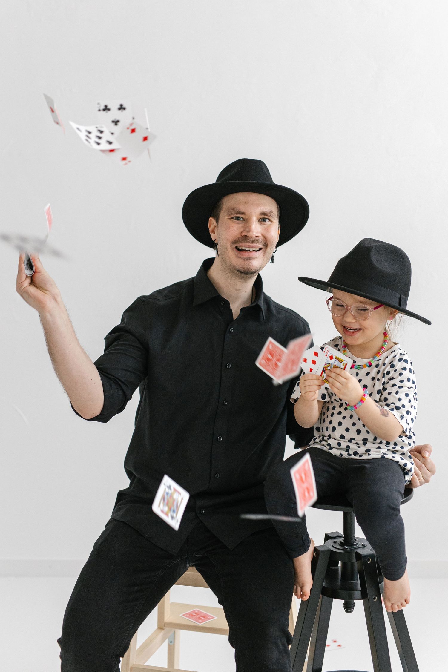 Father and child magicians performing card tricks together with floating cards.